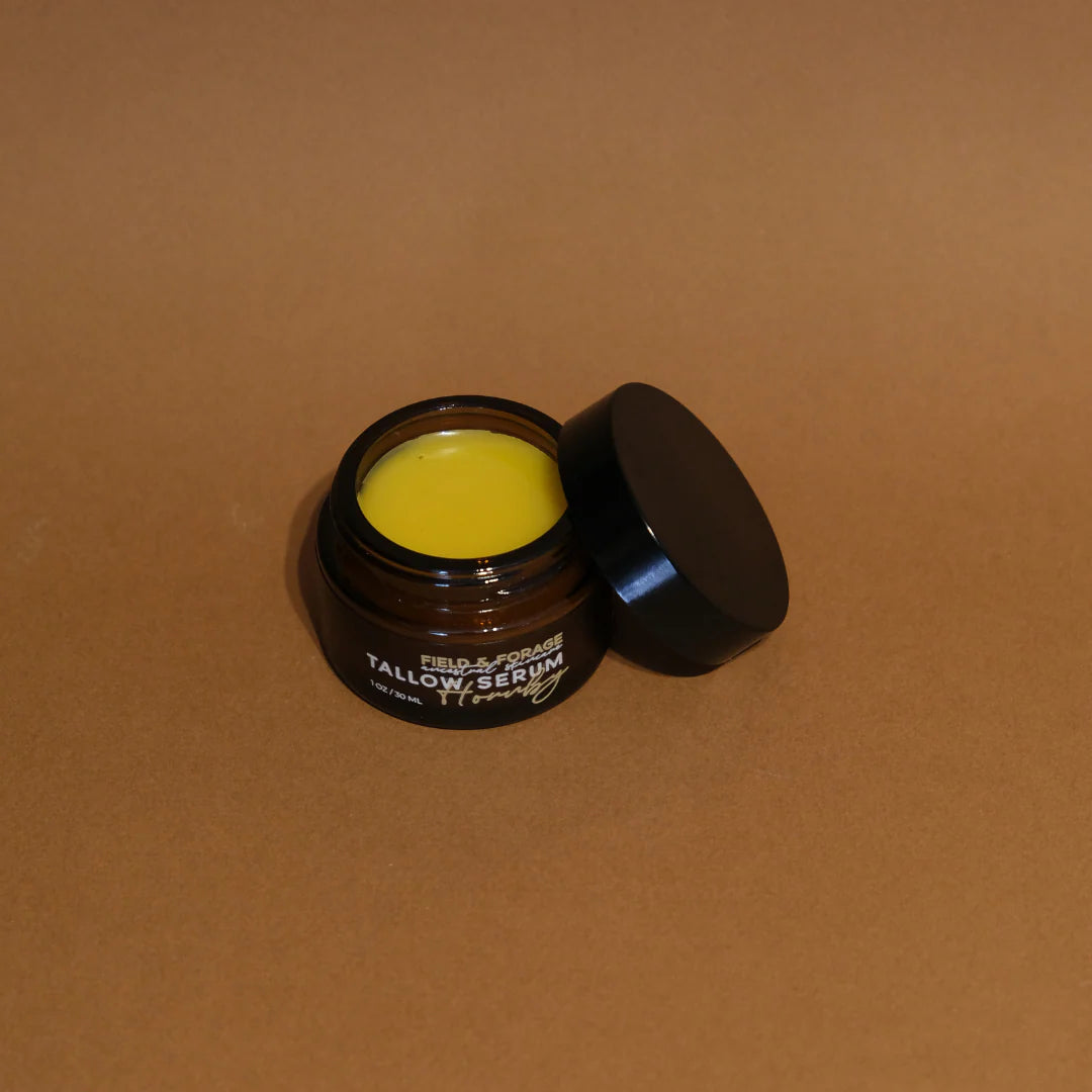 Jar of yellow Tallow face serum with a black lid on a brown background