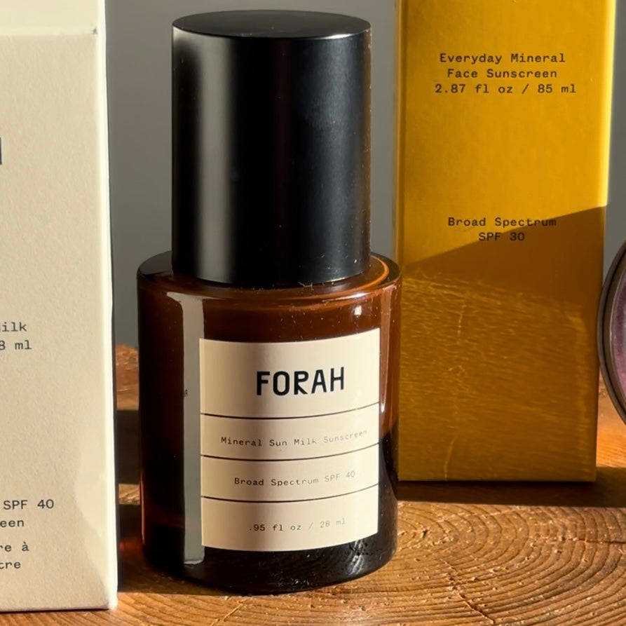 FORAH mineral sun milk sunscreen bottle on a wooden surface with other products in the background