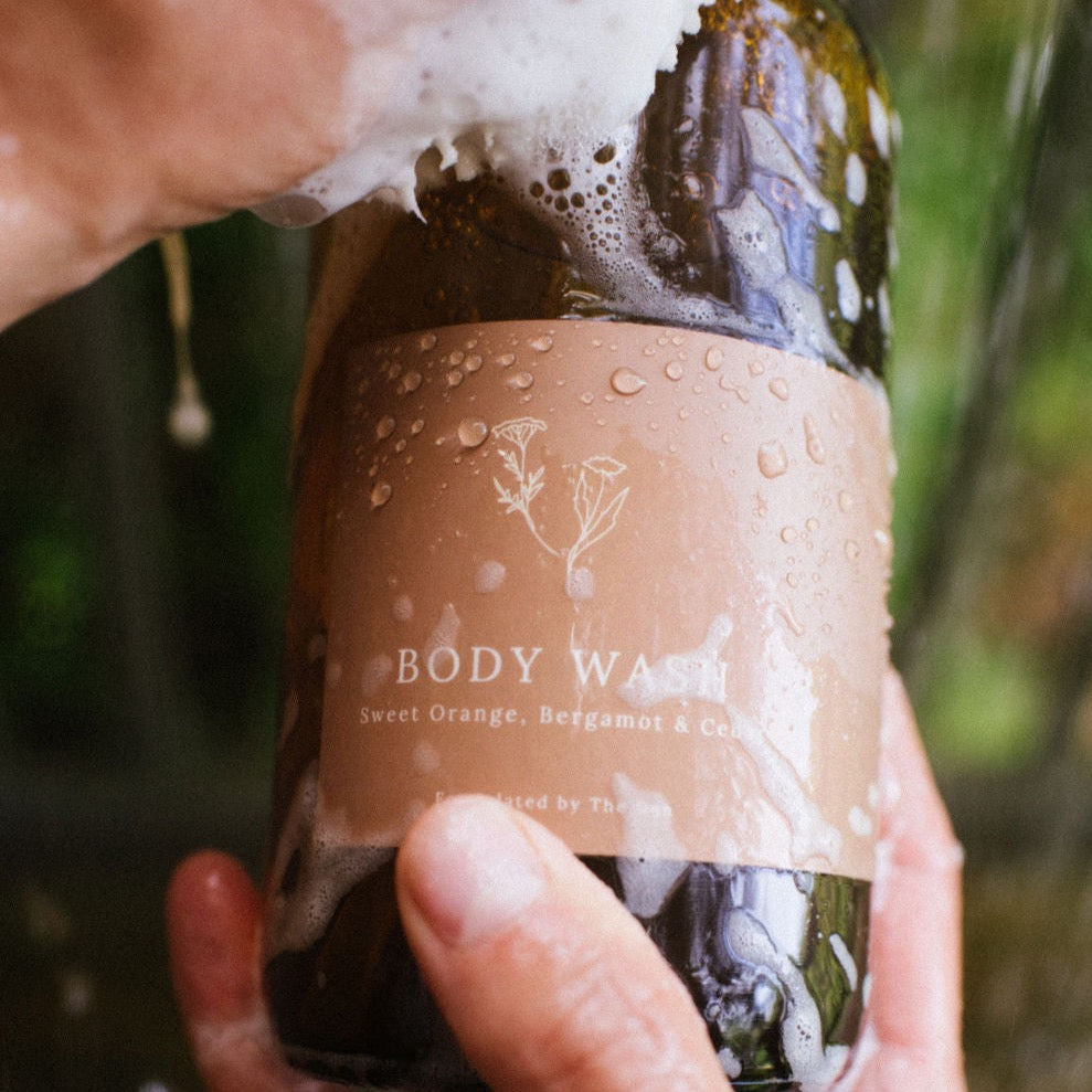 The Den Refillery body wash // hand soap in an amber glass bottle. Two hands hold it close to the camera as sudsy soap falls down the bottle.