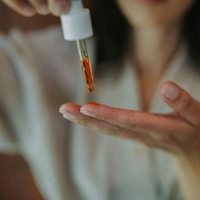 Person holding a dropper with a red liquid over a palm