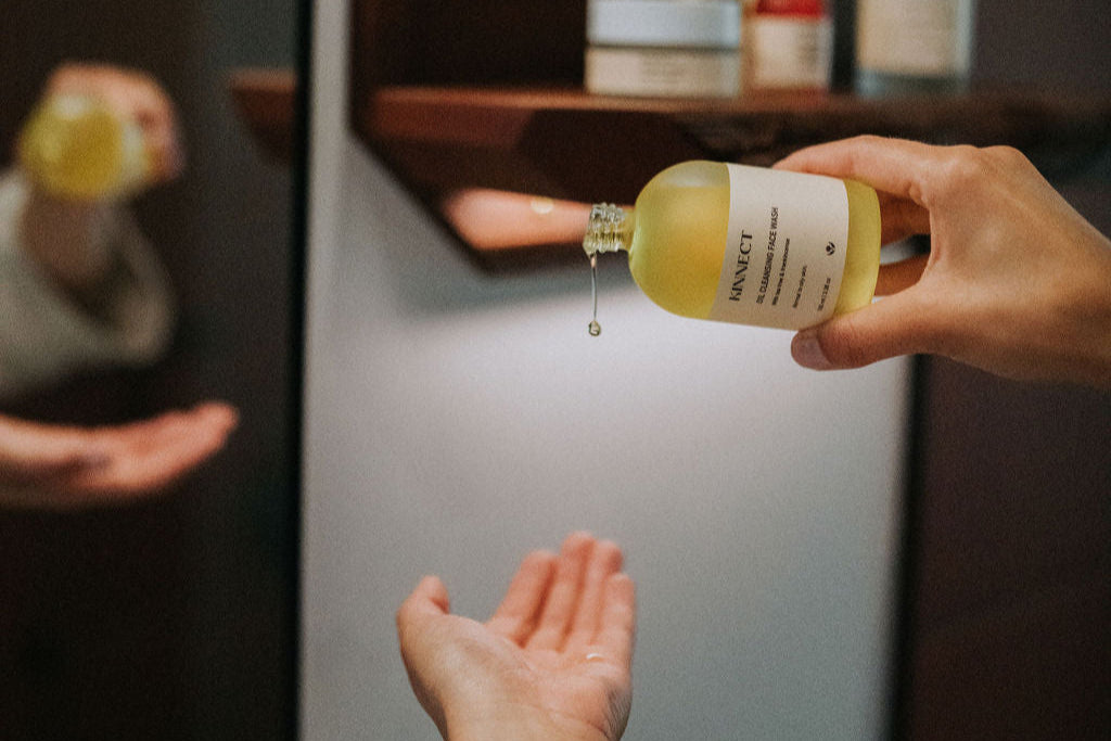 Person pouring a liquid from a bottle labeled Kinnect Oil Cleanser into their hand.
