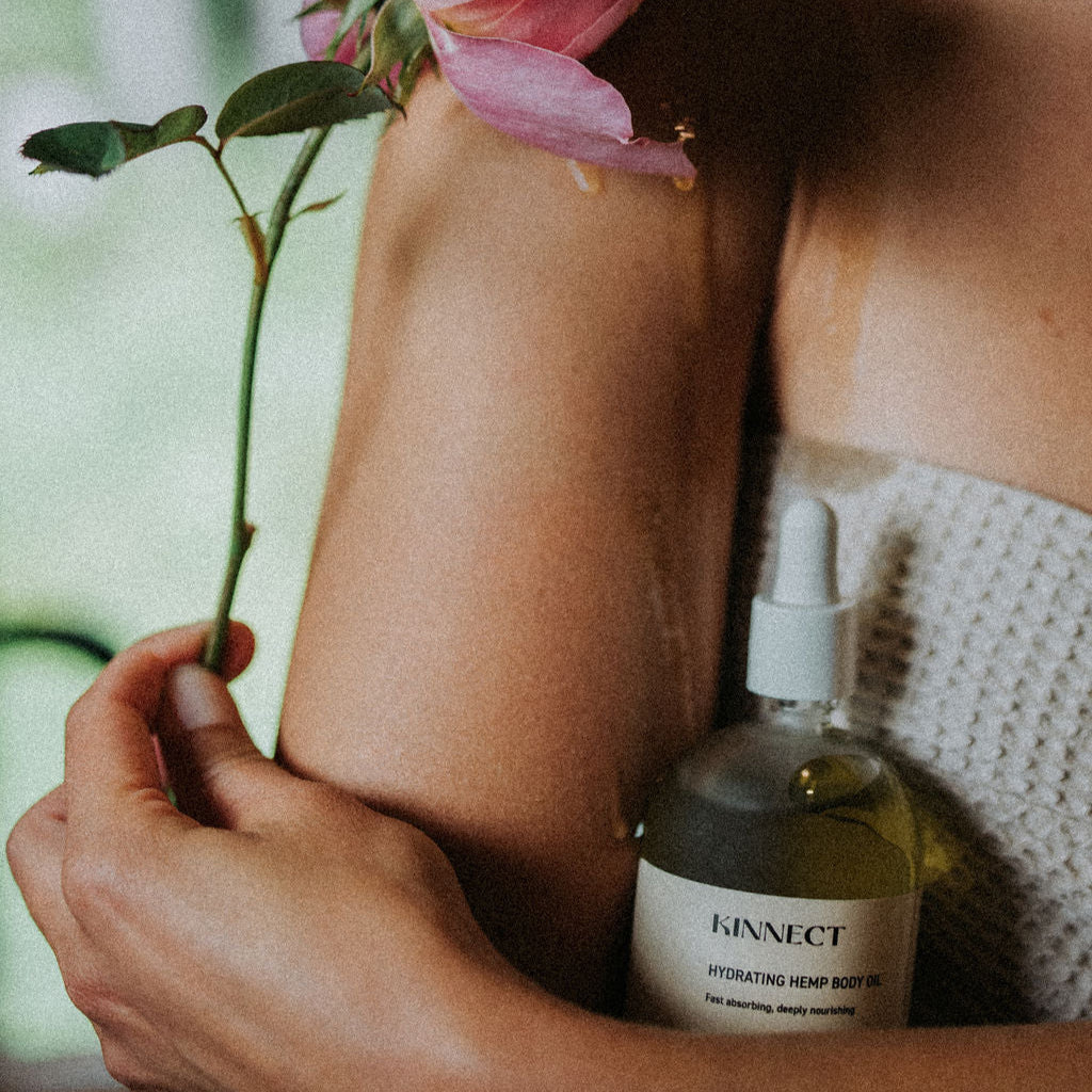 Person holding a pink flower and a bottle of Kinnect Hemp Body Oil with a blurred background