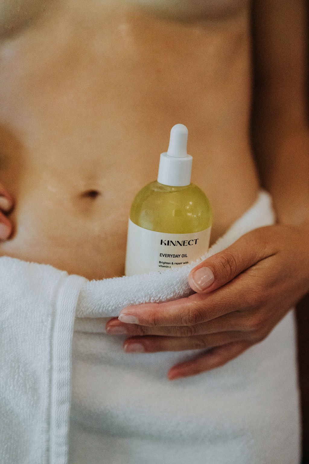 Person holding a bottle of Kinnect Everyday Oil with a towel around their waist.