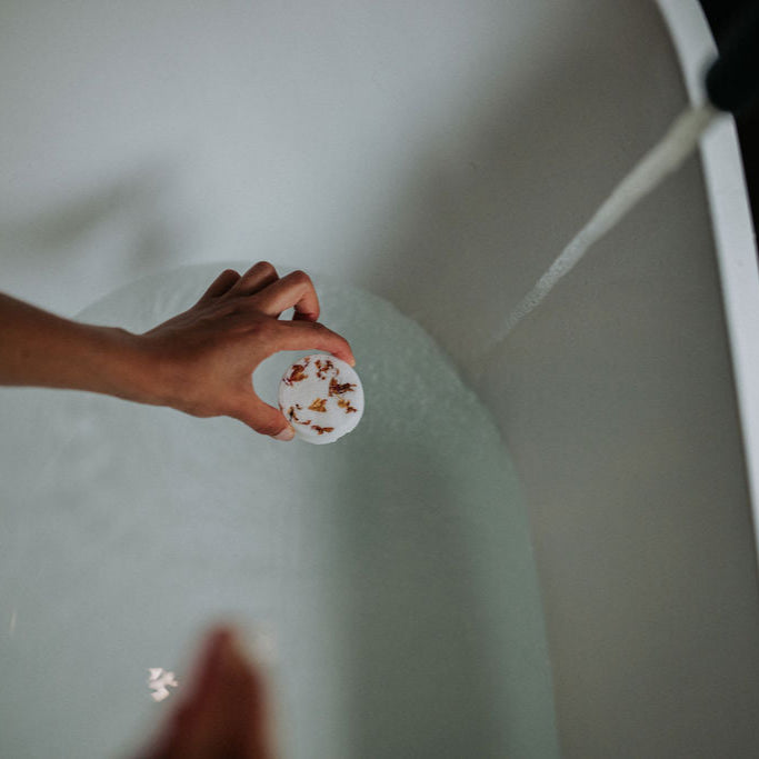 Ho wood and rose petal bath bomb held over running bath