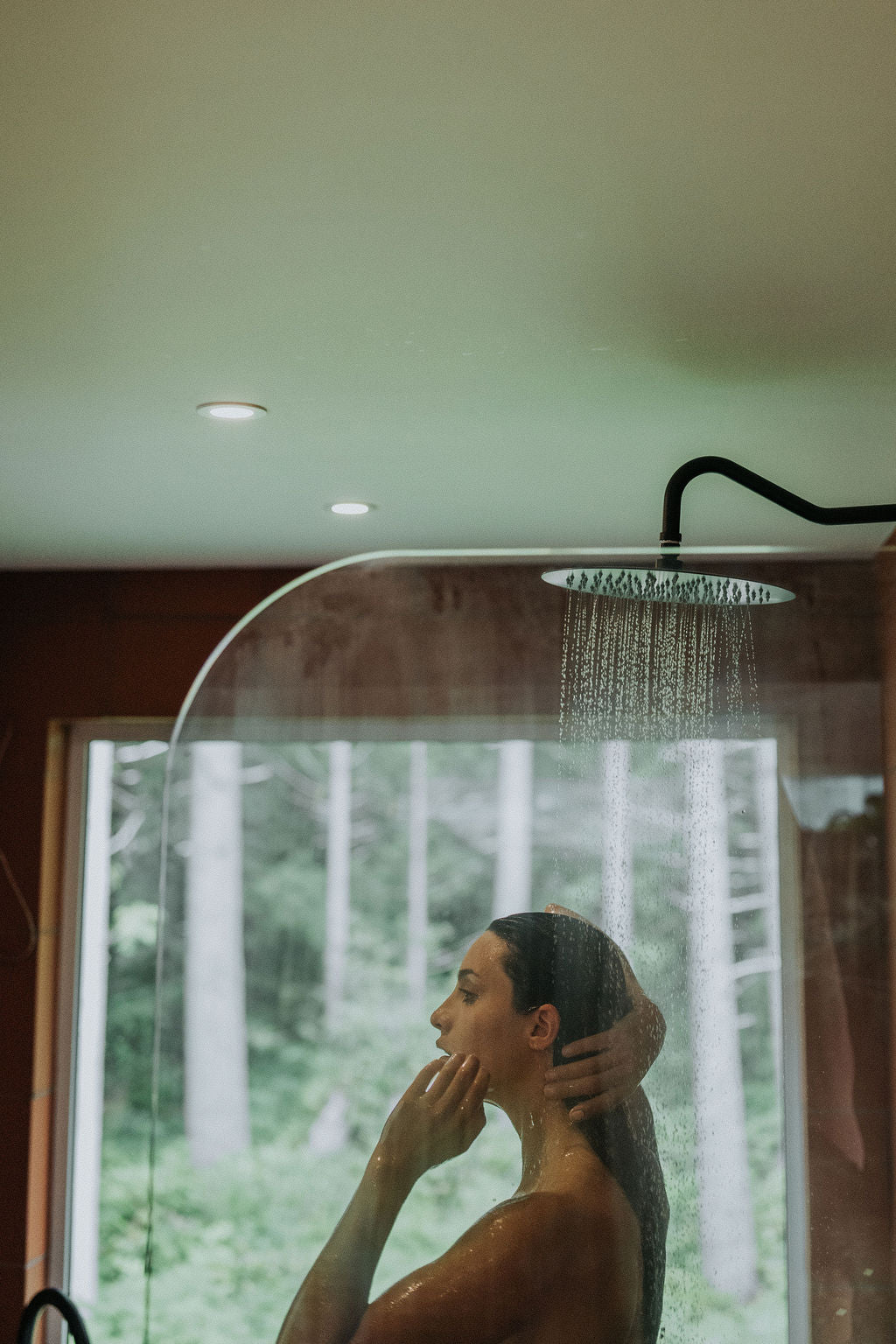 Person taking a shower with a forest view outside the window