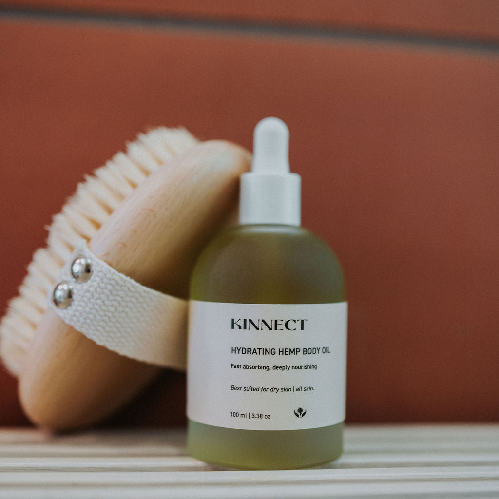 Kinnect hydrating hemp body oil bottle with a dry brush on a textured surface