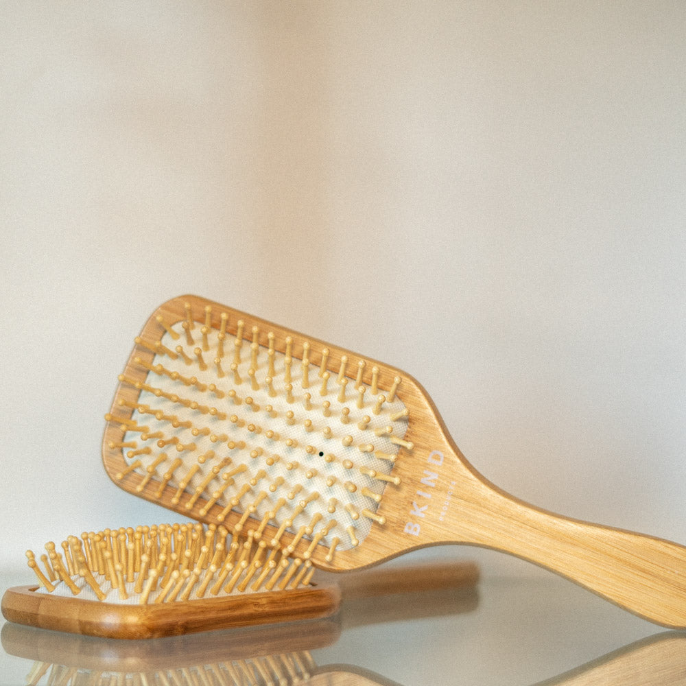 A Bamboo Hairbrush rests on a second bamboo hairbrush in a white room