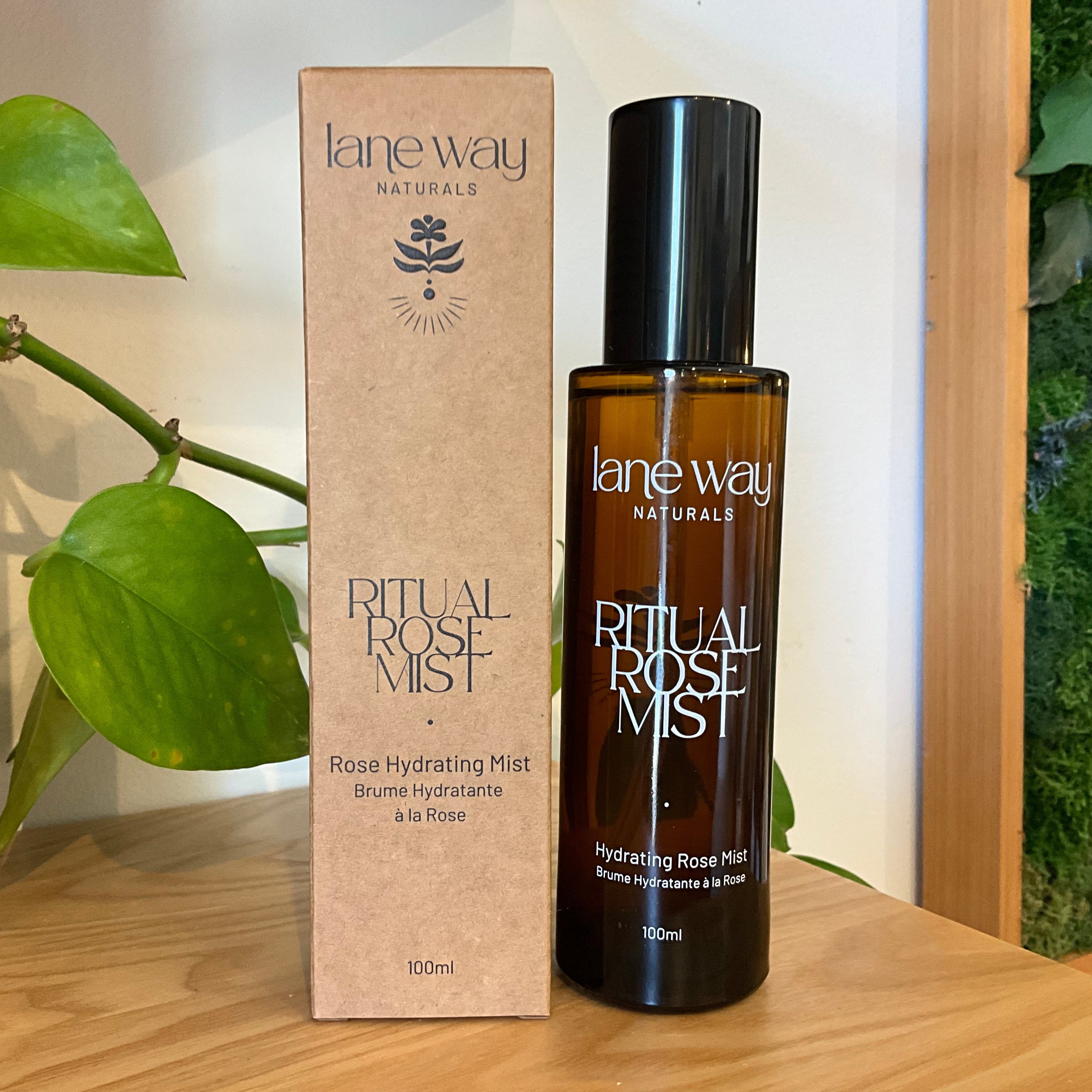 Lane Way Naturals Ritual Rose Mist bottle and matching kraft paper box displayed on a wooden surface with green plants in the background.
