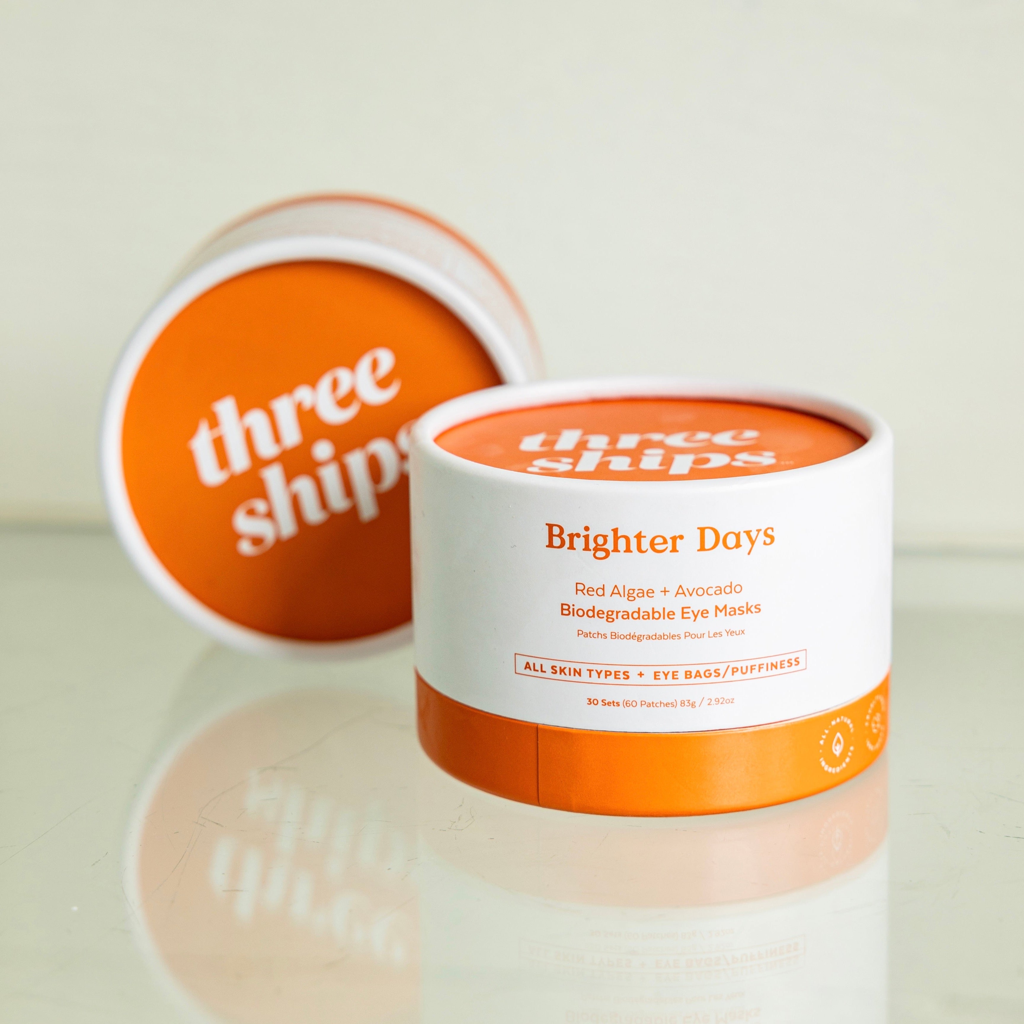Two packages of Three Ships Biodegradable eye masks sit on a glass surface so that the logo reflects below