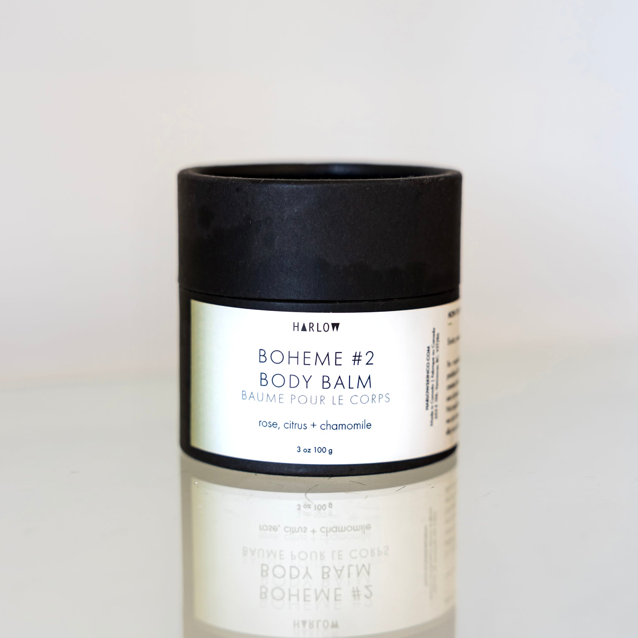 Bohème Body Balm by Harlow sits on a glass surface so that the product packaging reflects below