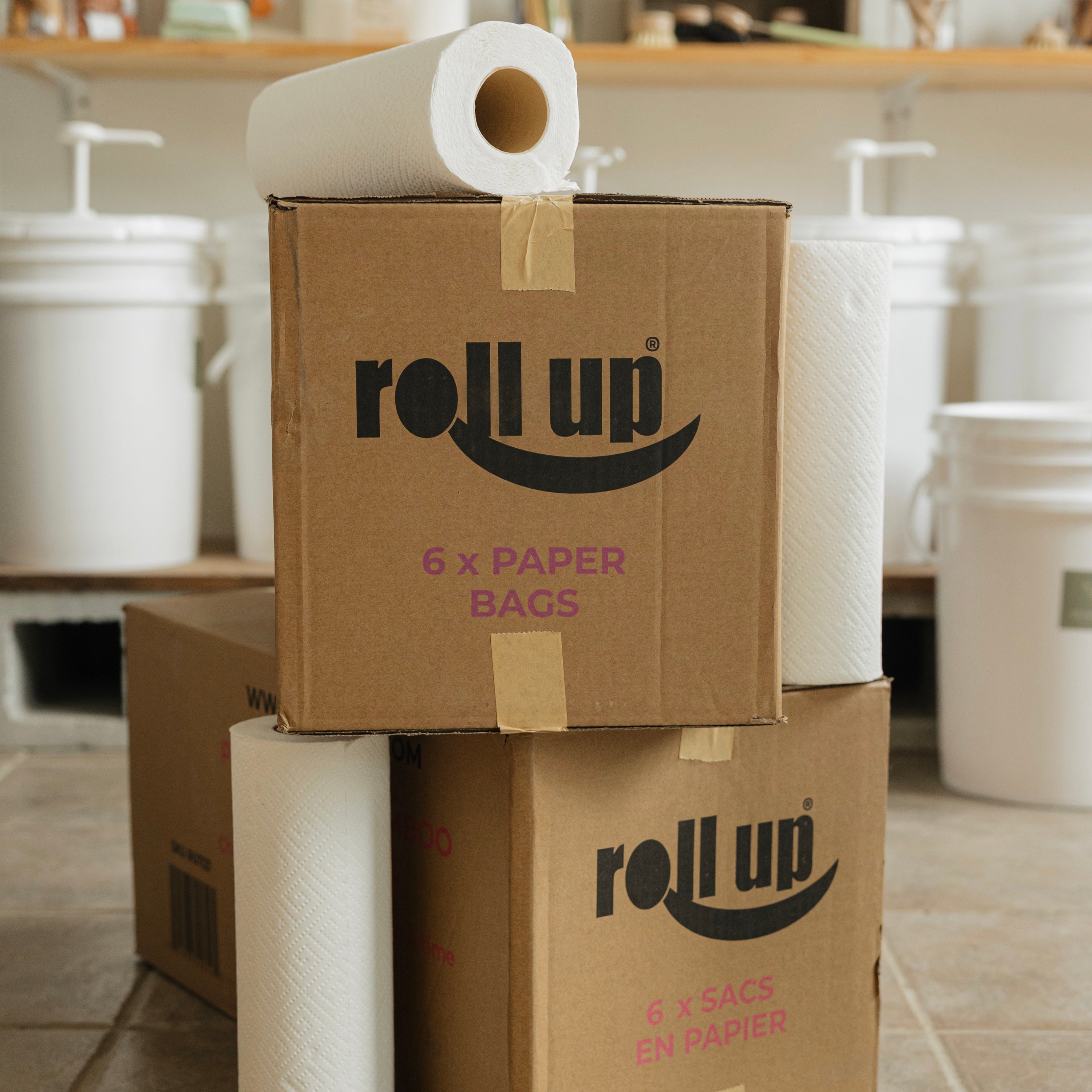 Cardboard boxes with 'roll up' branding and paper bags on a tiled floor.
