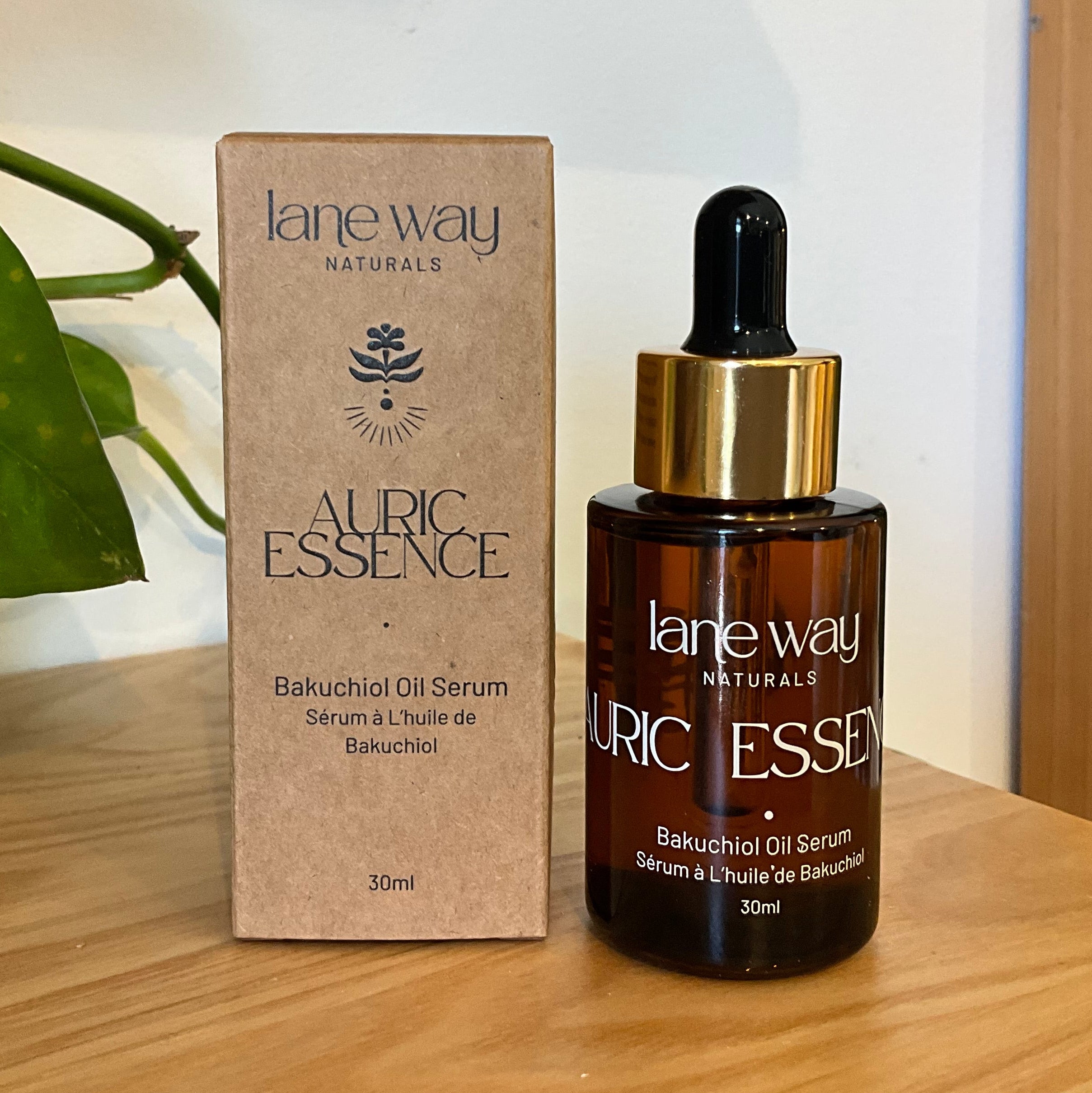 Lane Way Naturals Auric Essence Balunchool Oil Serum in a 30ml amber glass dropper bottle next to its kraft paper packaging box, displayed on a wooden surface with a green plant in the background.