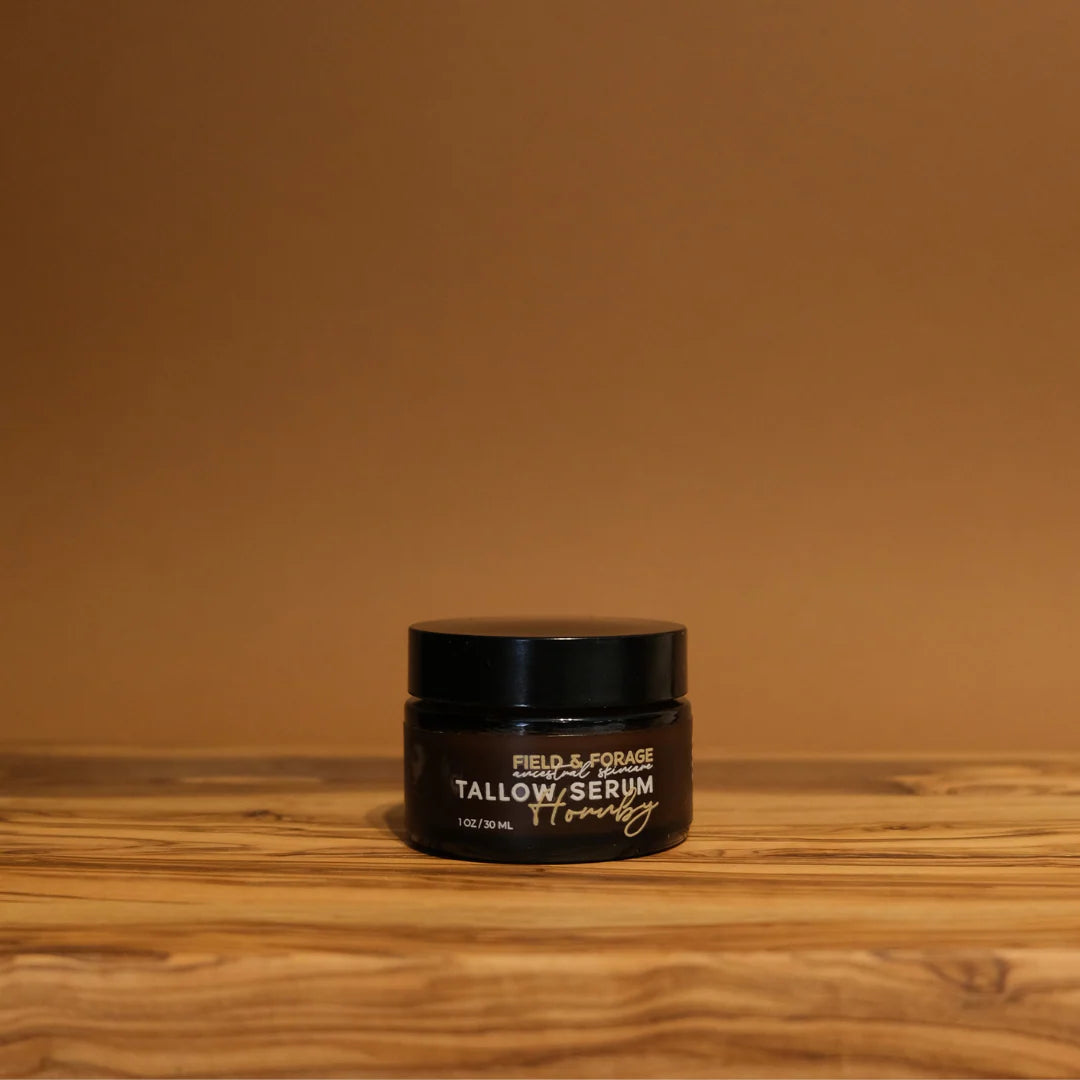 Black jar of Tallow Face Serum on a wooden surface with a brown background
