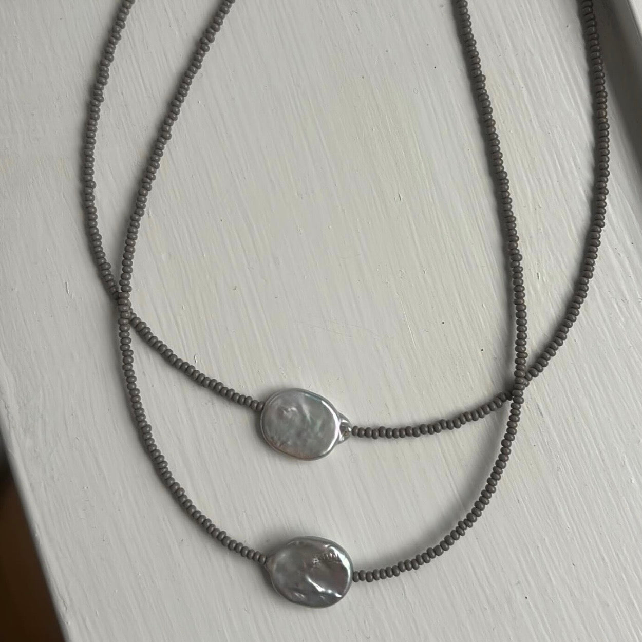 Two silver necklaces with round pendants on a light wooden surface