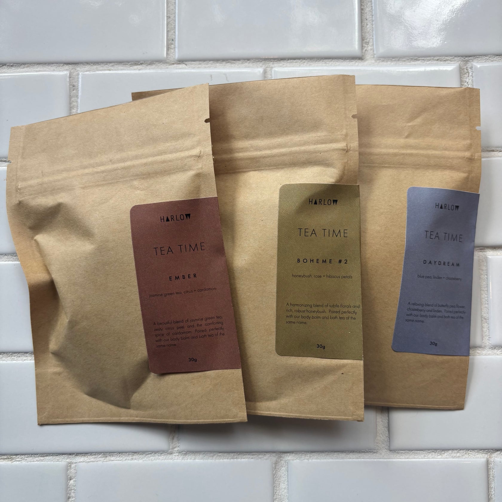 Three brown paper tea bags with labels on a tiled wall background