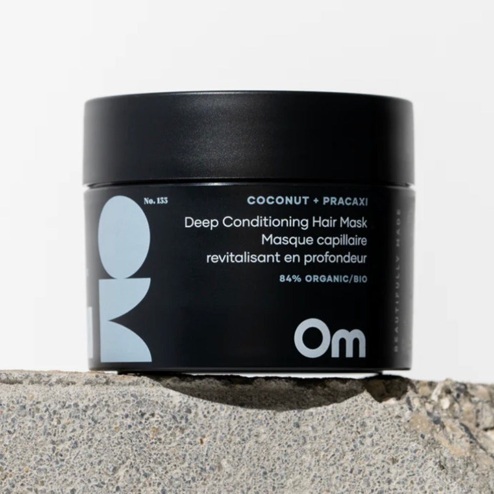Black hair mask jar with 'Om' branding on a stone surface