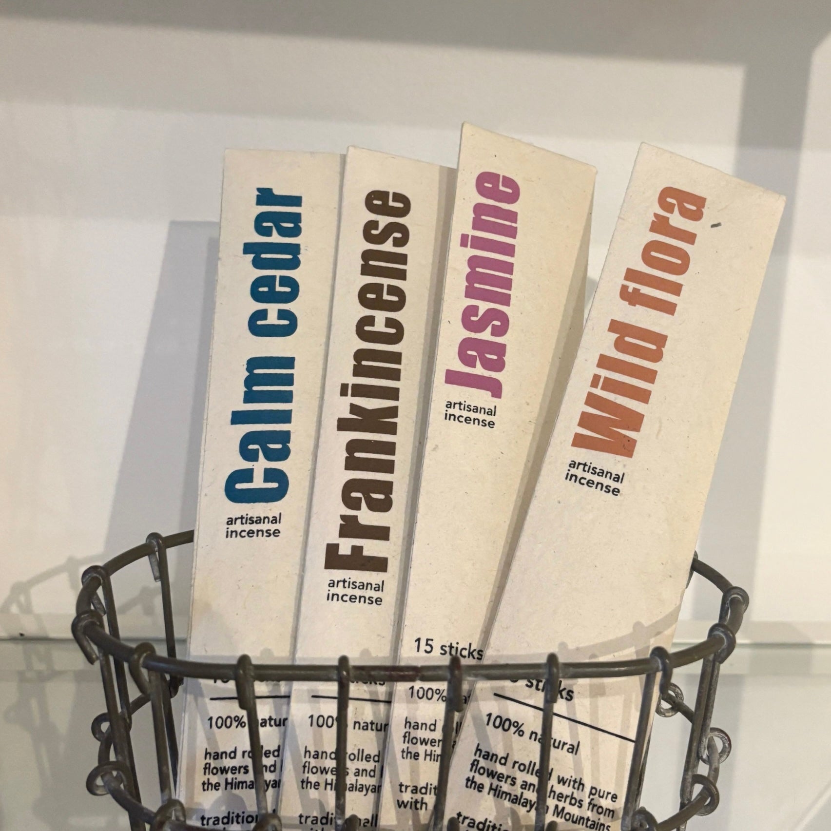 Four packs of artisanal incense labeled 'Calm Cedar', 'Frankincense', 'Jasmine', and 'Wild Flora' in a wire basket.