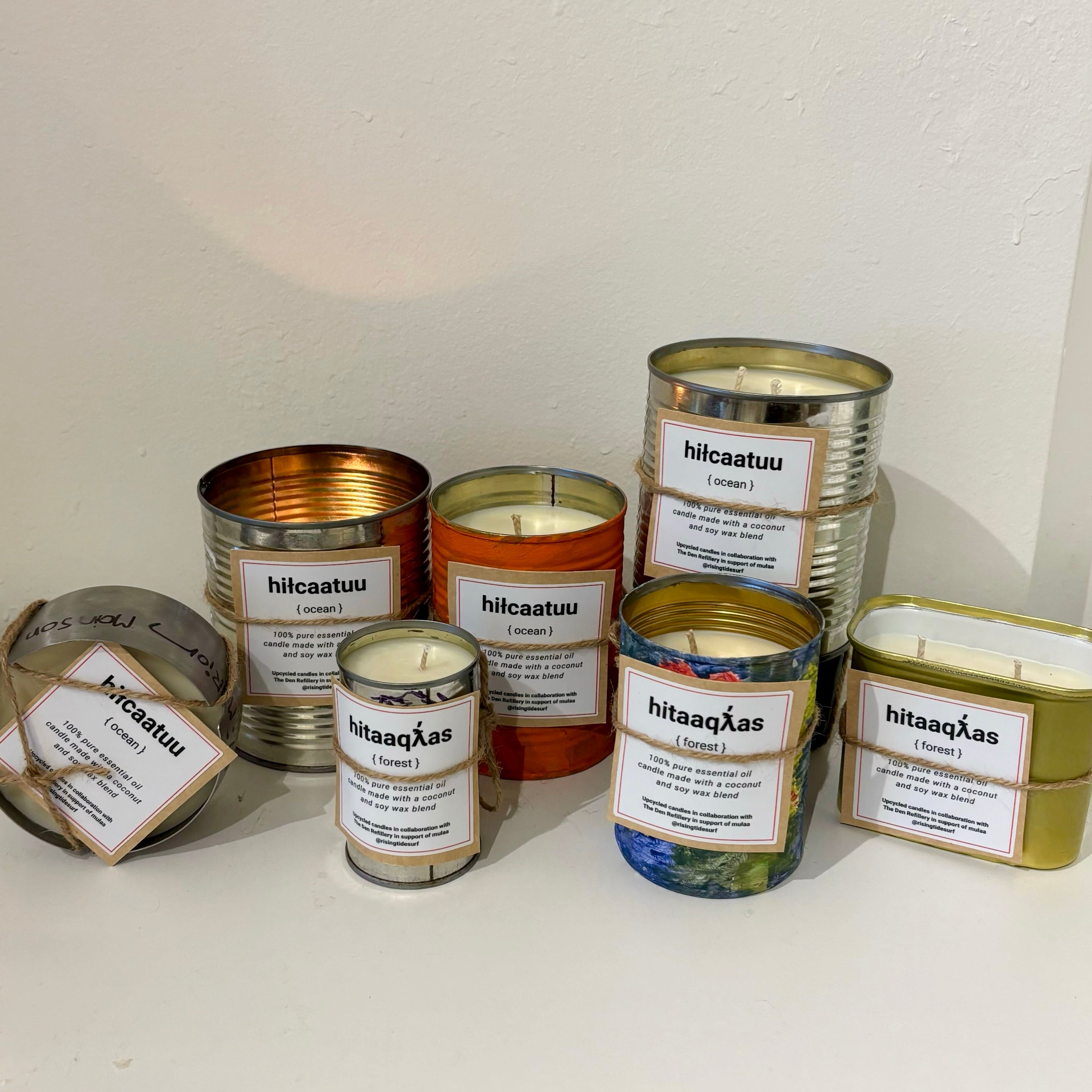 Collection of candles in various tins with labels on a white surface.