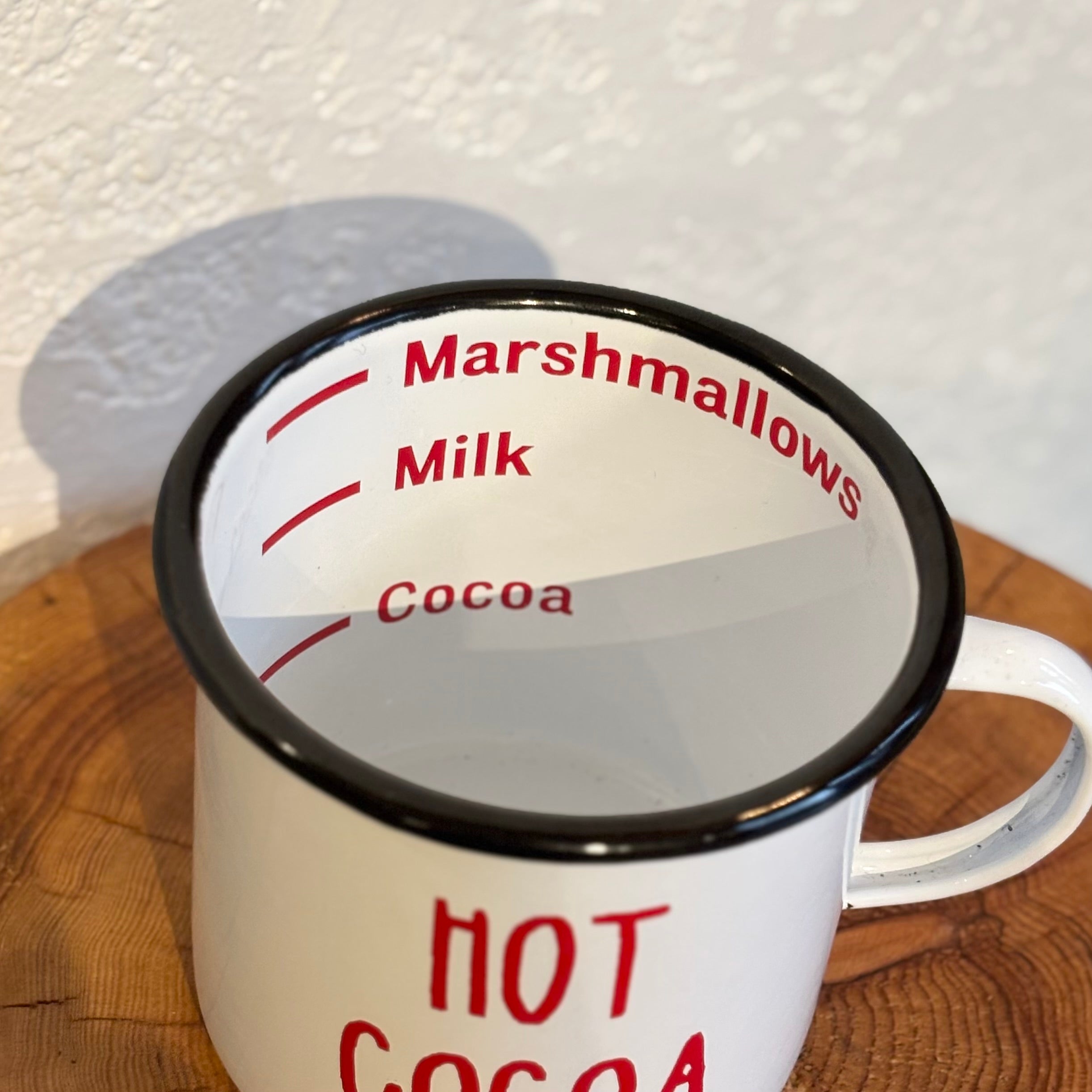 White mug with black rim and red text for making hot cocoa, on a wooden surface.