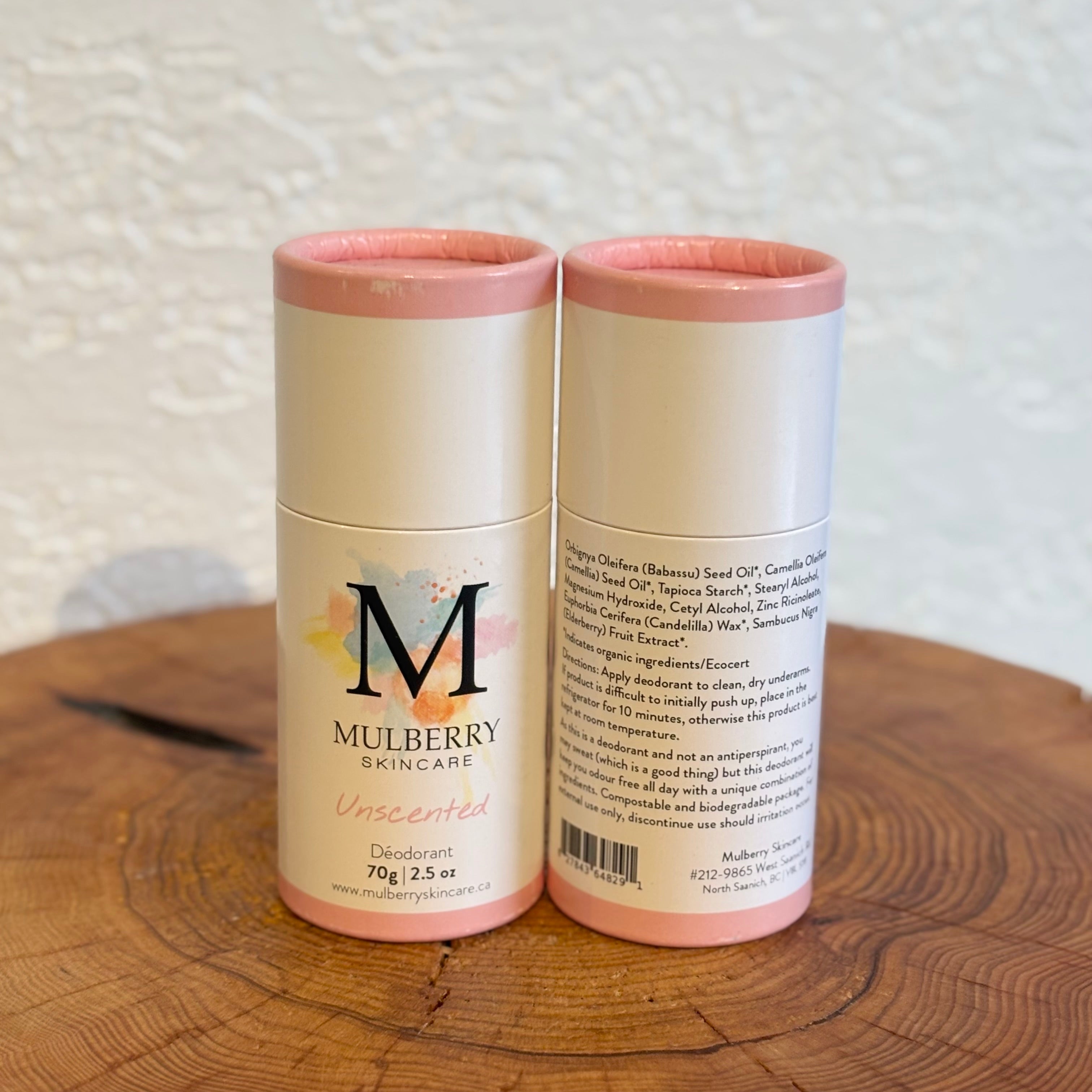 Two cylindrical Mulberry Skincare deodorant containers on a wooden surface with a textured white wall background.