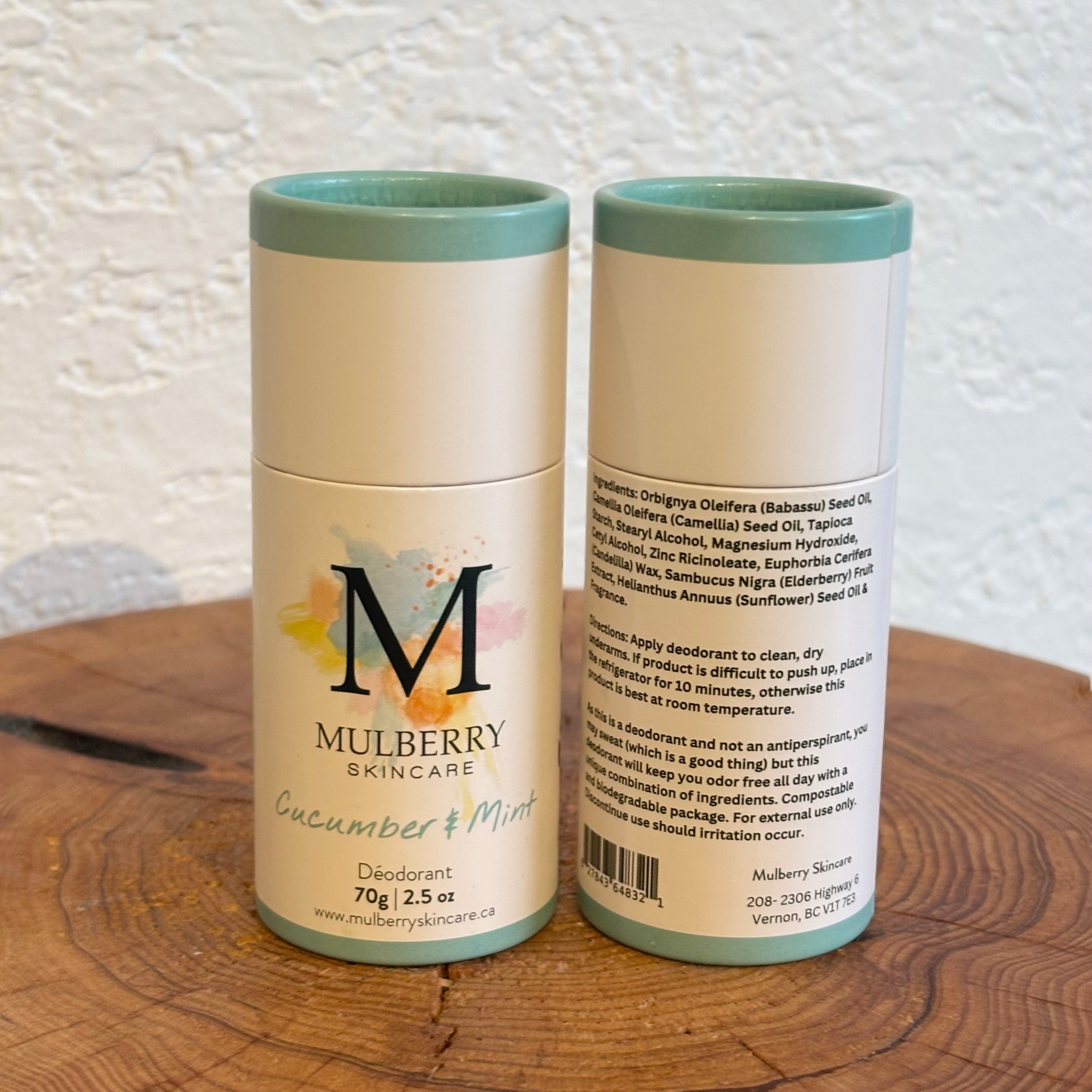 Two Mulberry Skincare deodorant cans on a wooden surface with a textured white wall background.