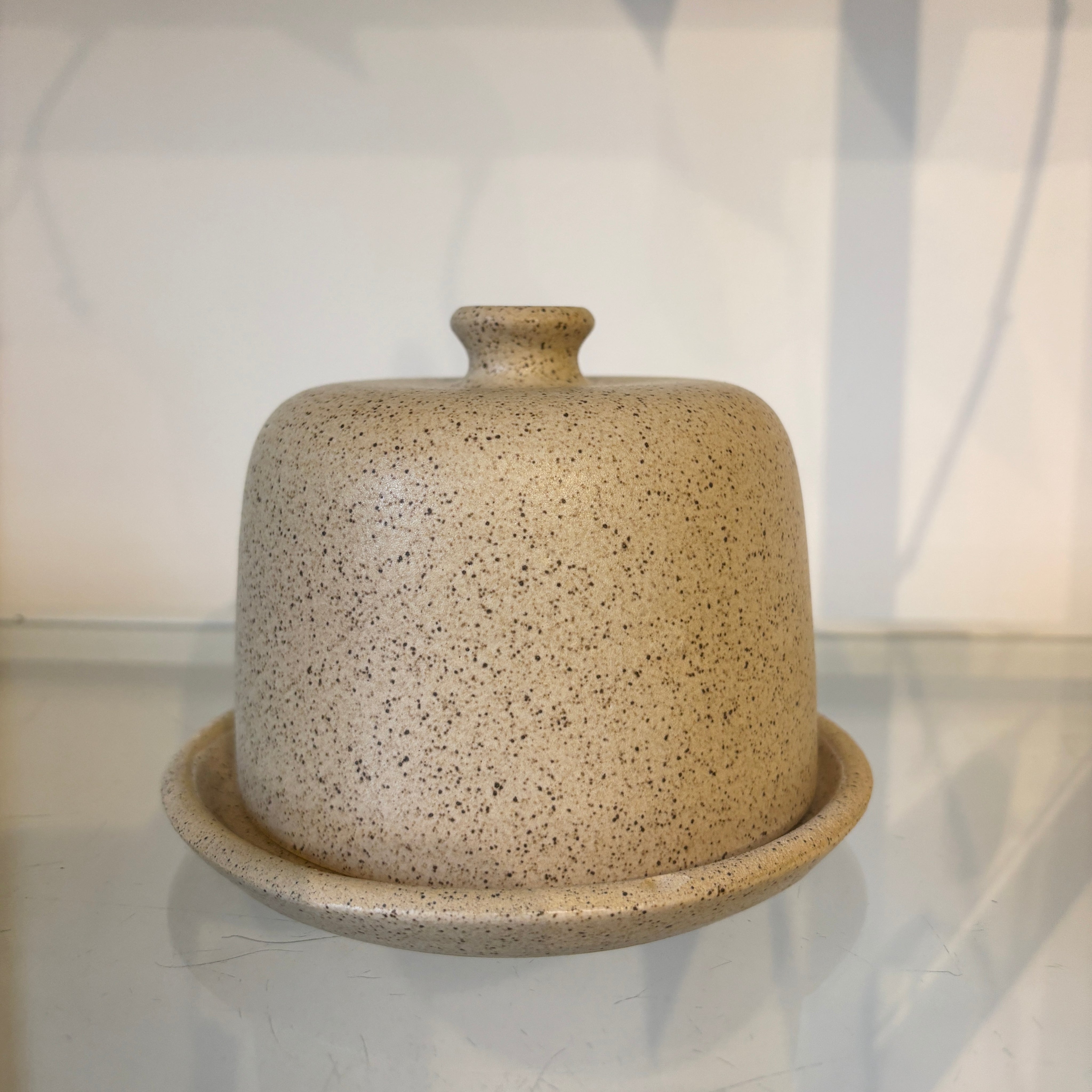 Speckled beige ceramic butter dish with base on a reflective surface