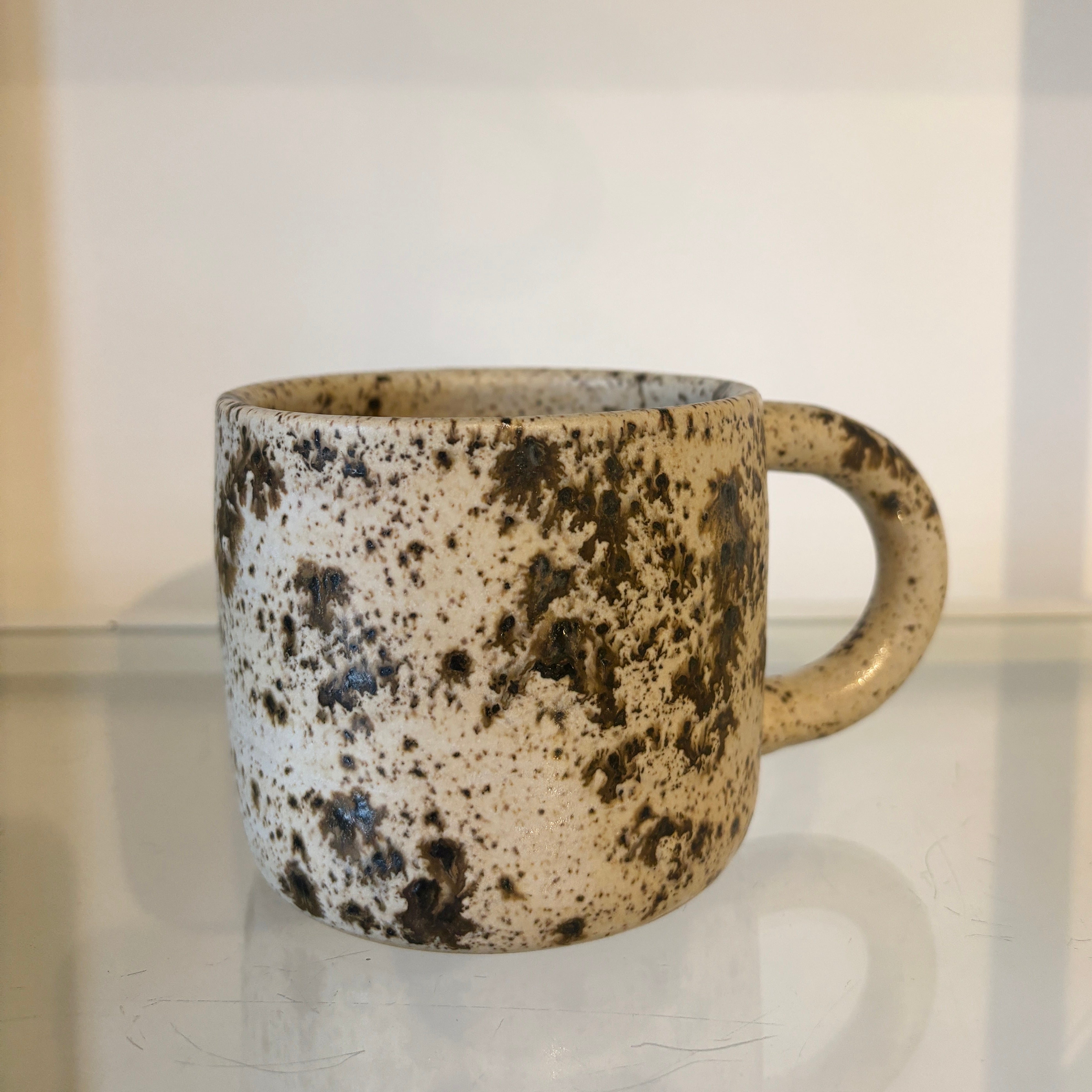 Speckled ceramic mug on a reflective surface with a neutral background