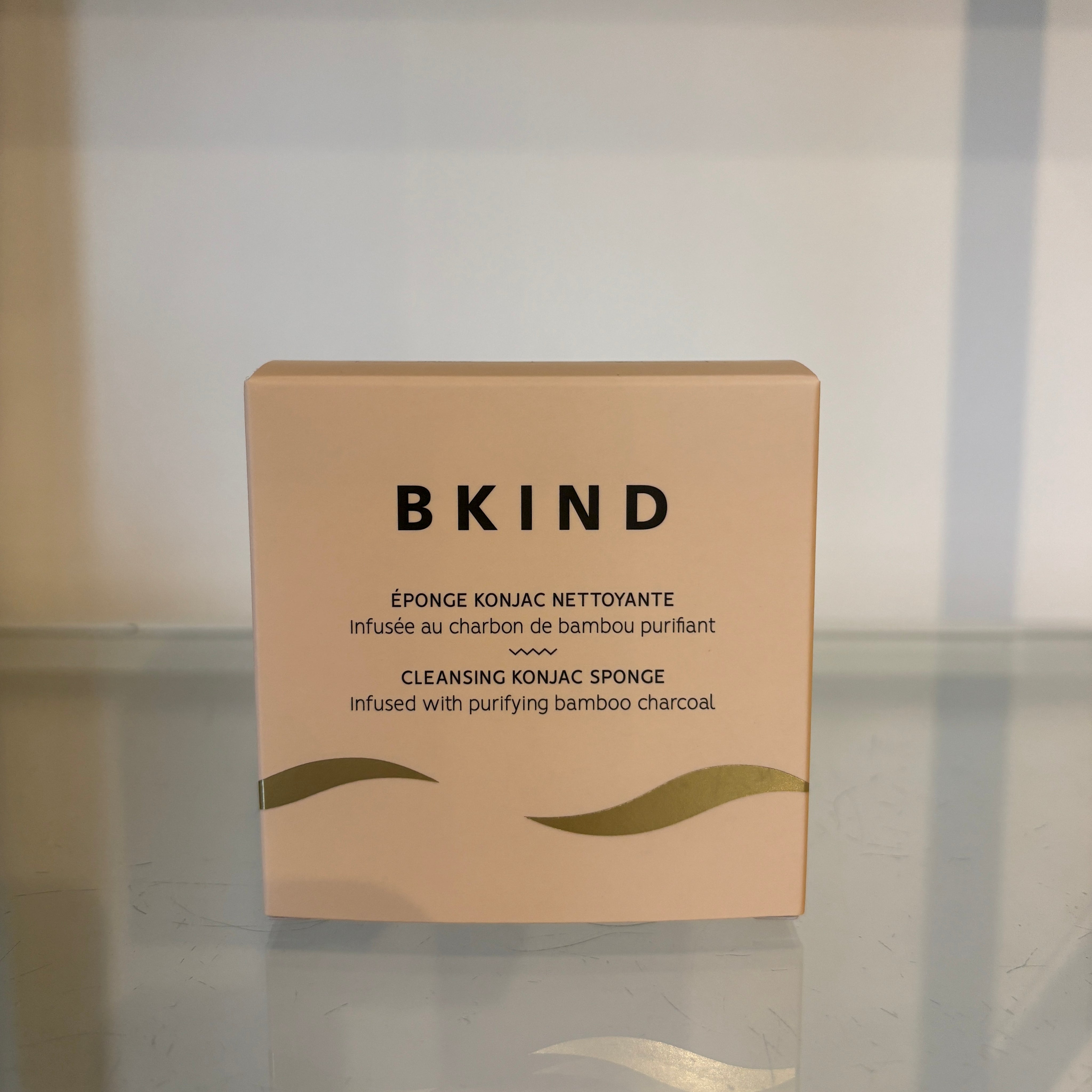 Box of BKIND cleansing konjac sponge on a reflective surface with a neutral background