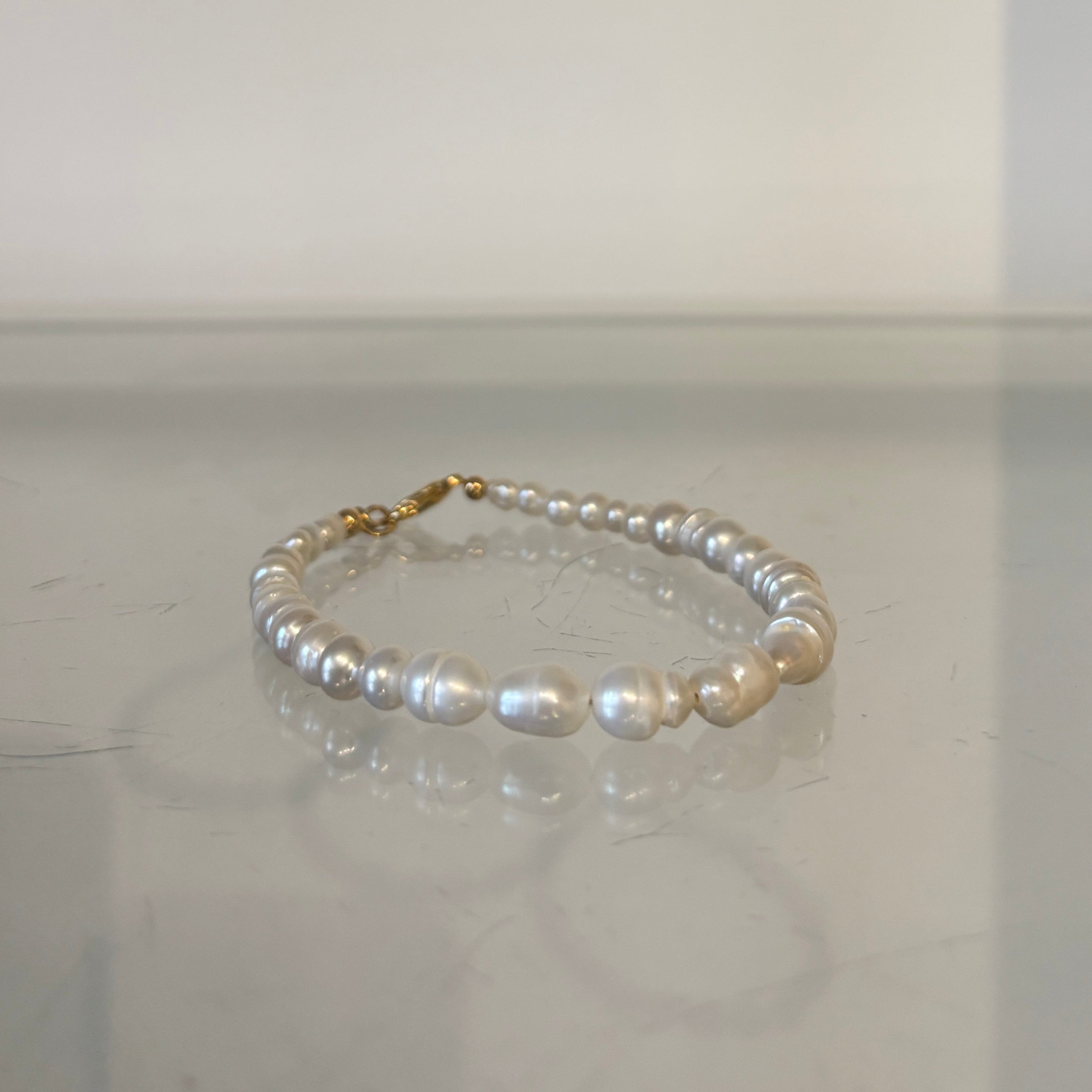 Pearl bracelet with gold clasp on a reflective surface
