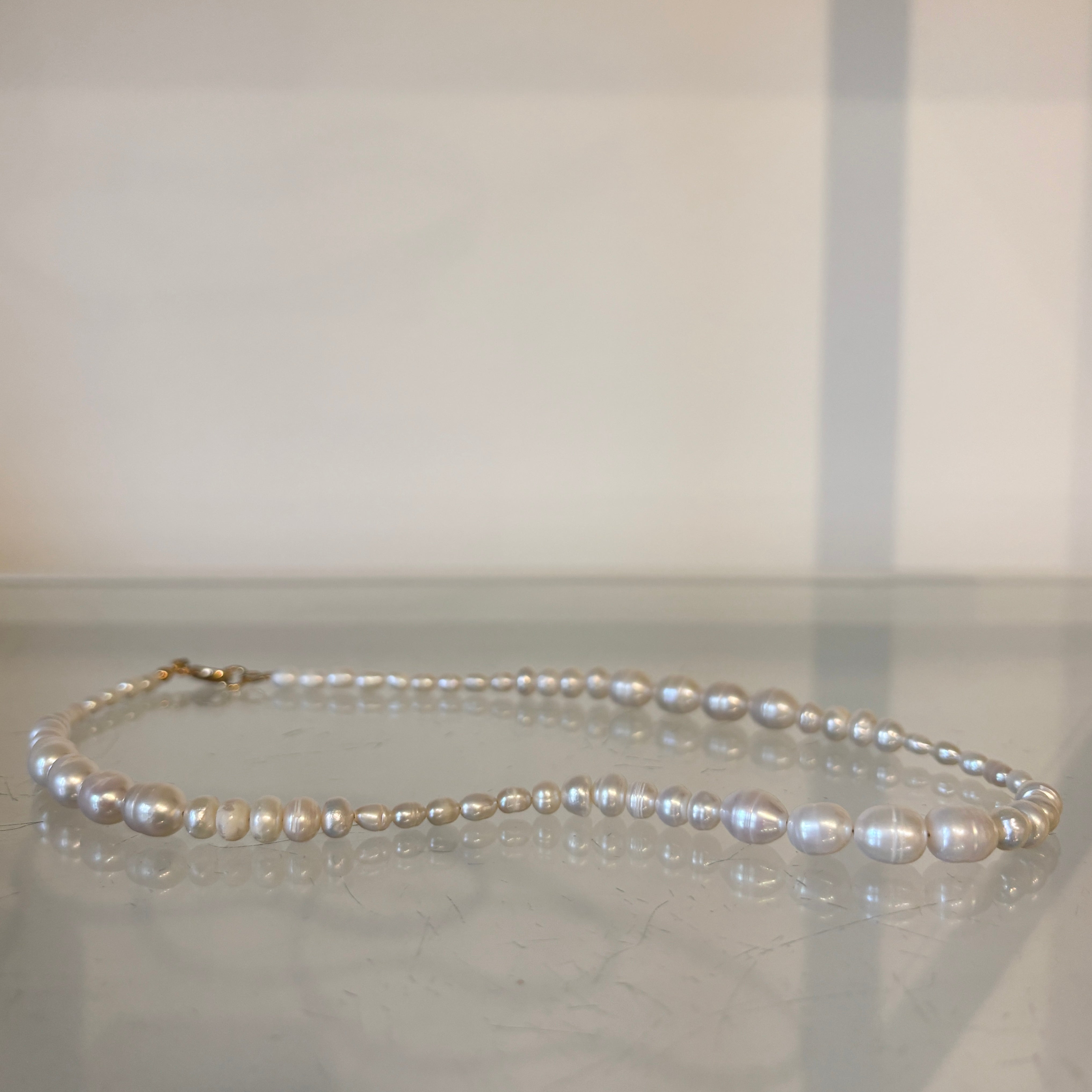 Pearl necklace on a reflective surface with a neutral background