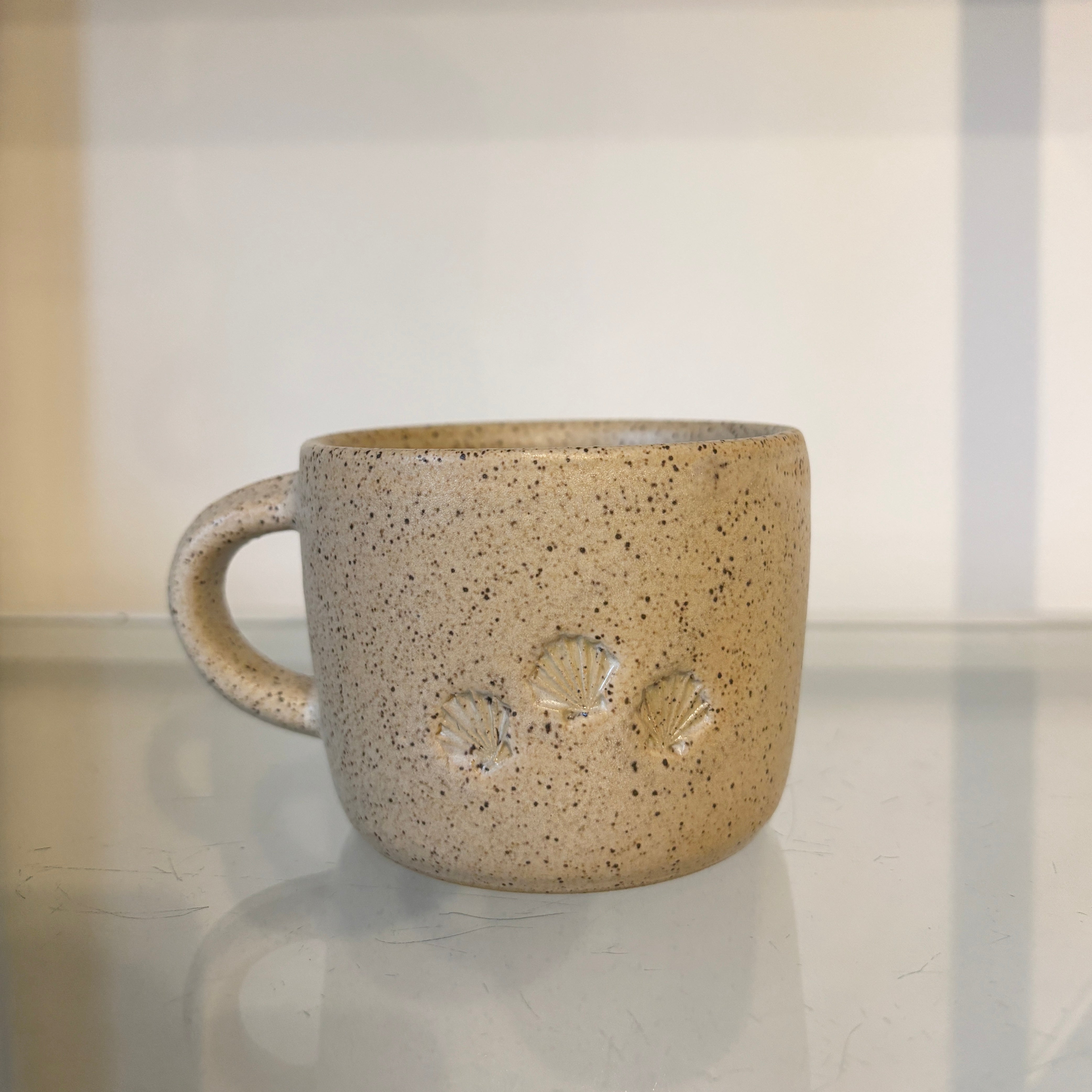Speckled ceramic mug on a reflective surface with a neutral background