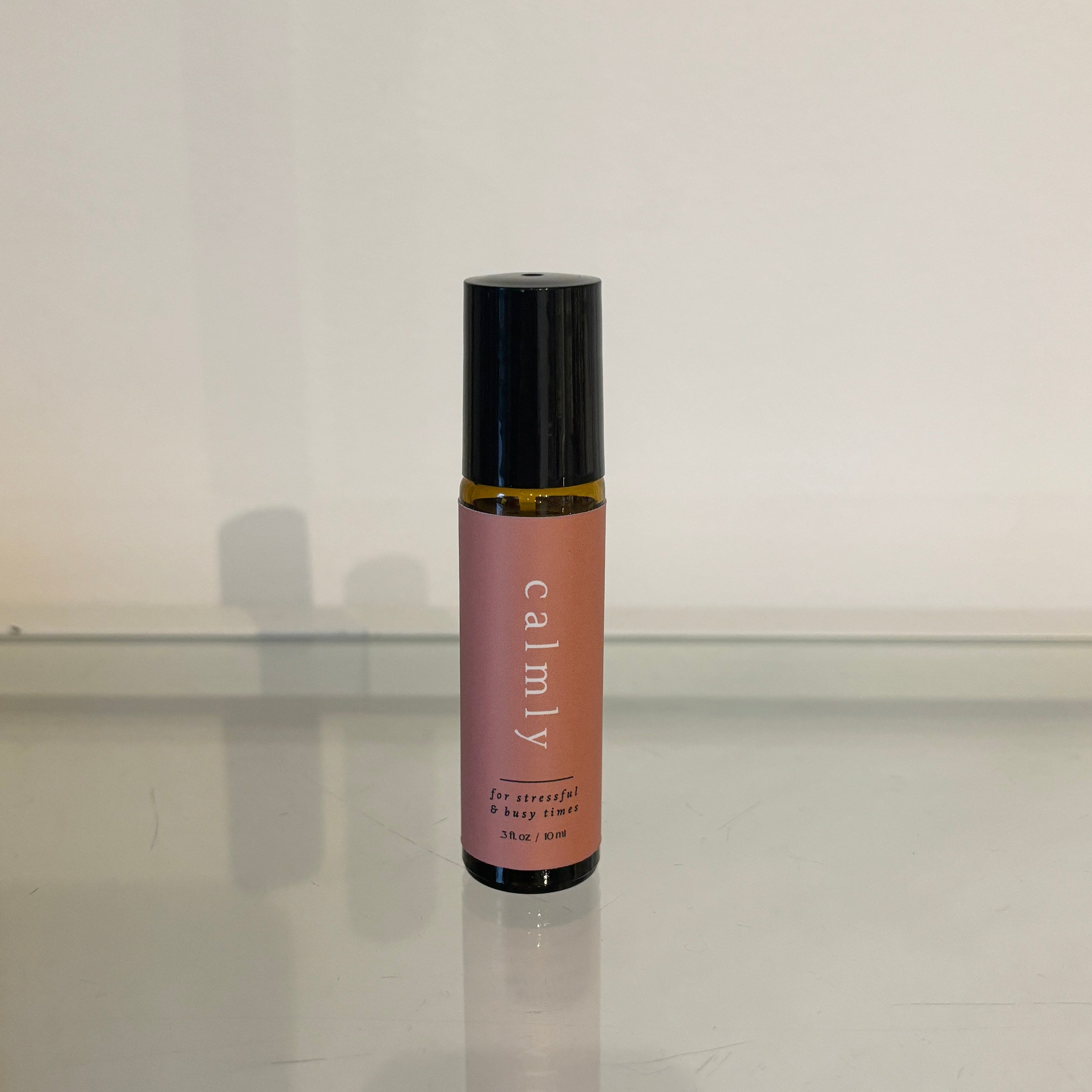 Roll-on bottle with pink label and black cap on a reflective surface.