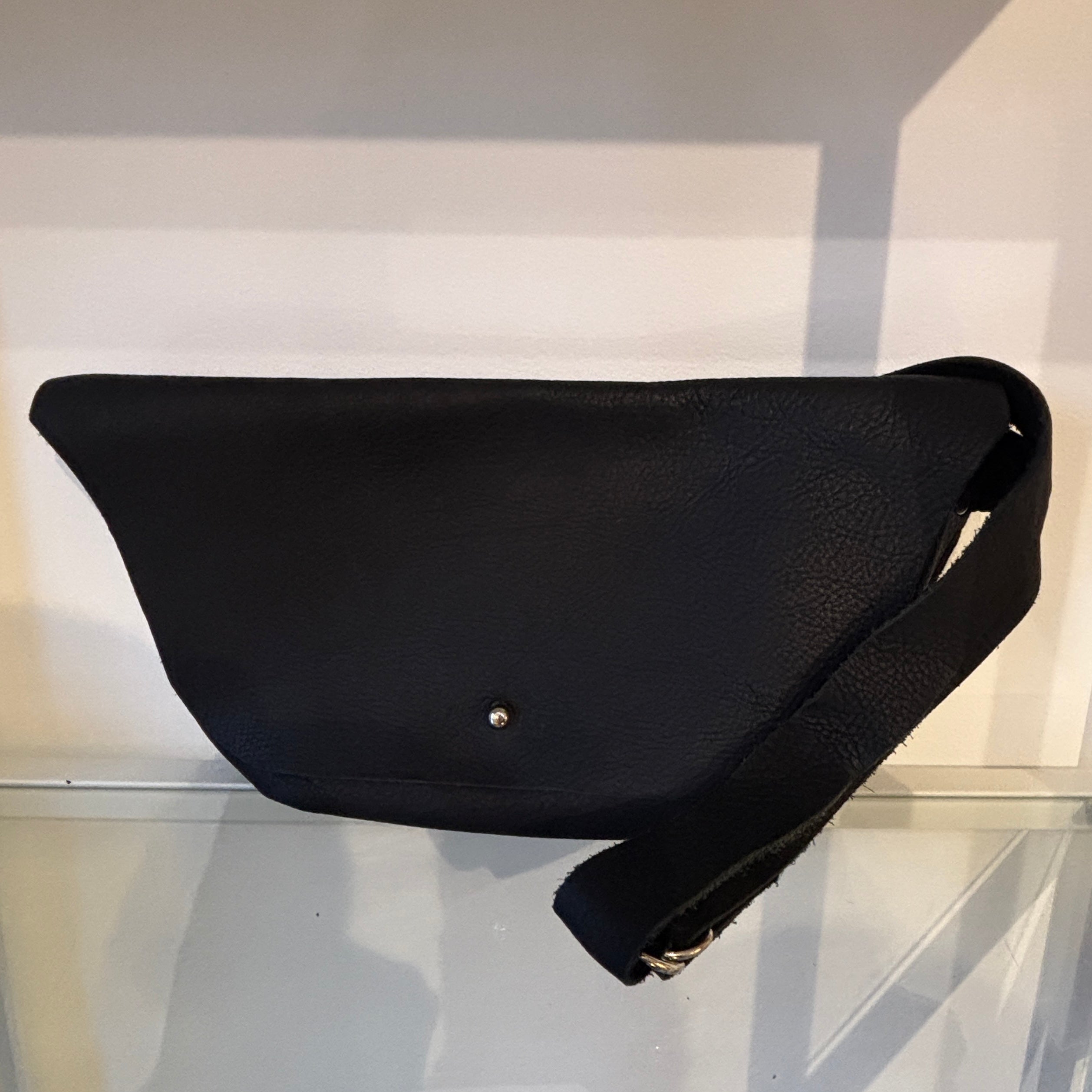 Black waist bag on a reflective surface with a white background