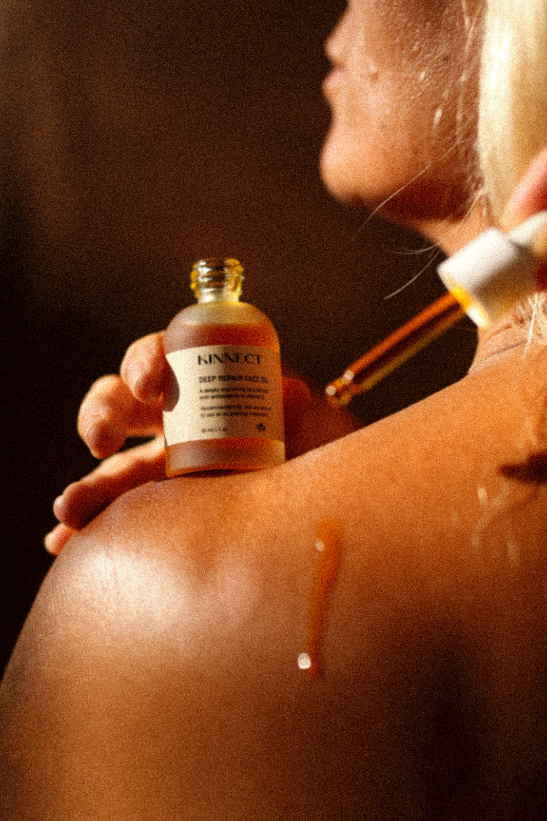 Person applying a Kinnect Deep Repair skincare oil to their shoulder with a dropper bottle.