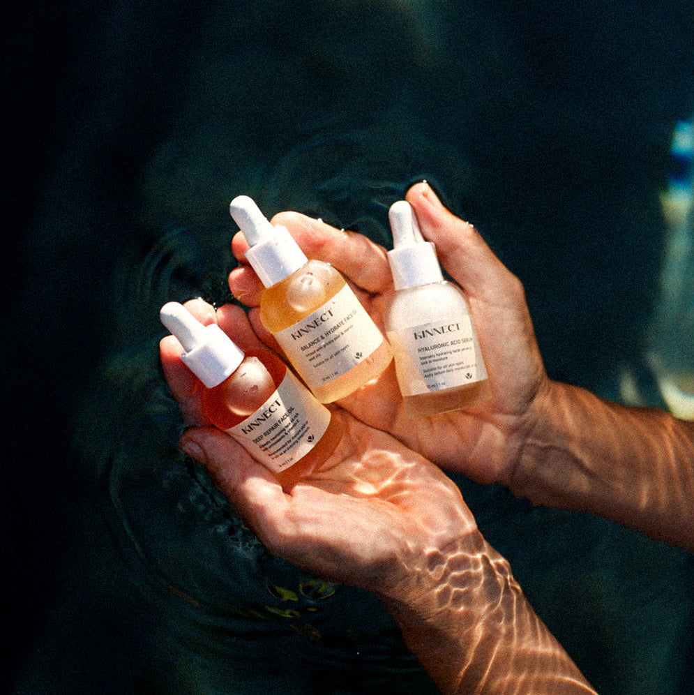 Hand holding three skincare bottles with a blurred underwater background