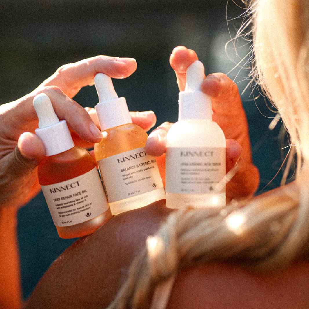 Person holding skincare bottles with a blurred outdoor background