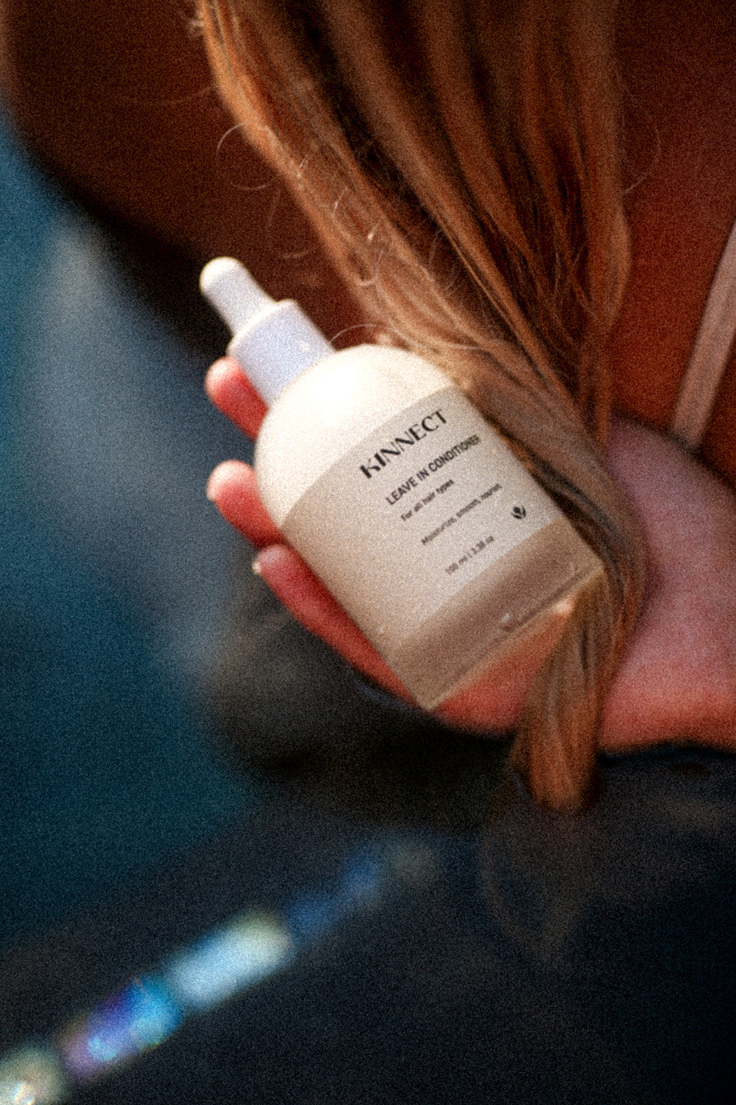 Hand holding a skincare bottle labeled 'KINNECT Leave in Conditioner' with blurred background
