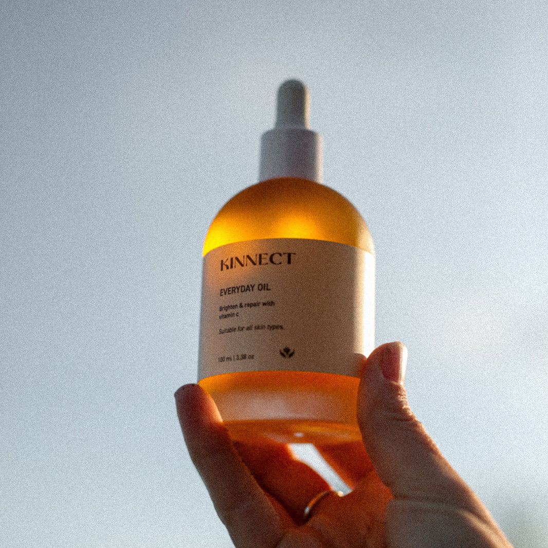 Hand holding a bottle of Kinnect skincare product against a light background