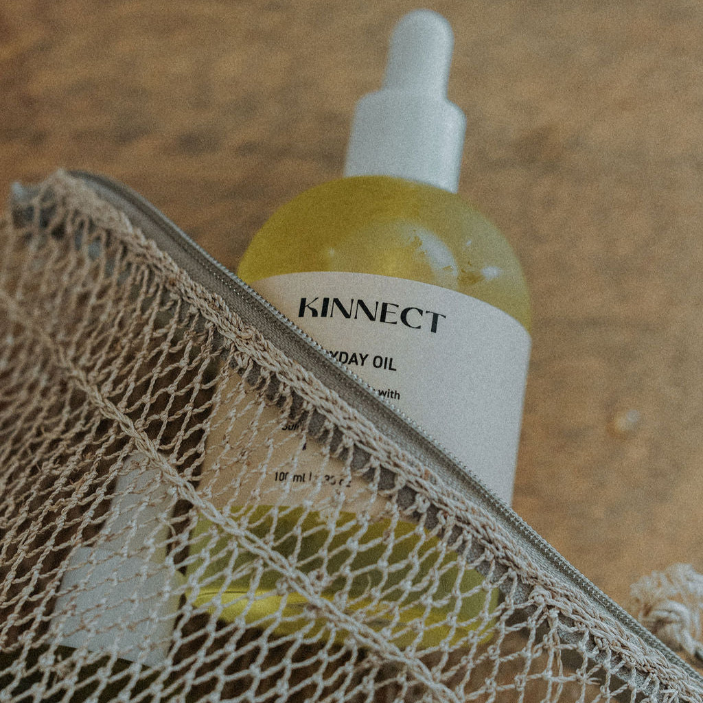Bottle of Kinnect Everyday Oil with a dropper in a textured bag