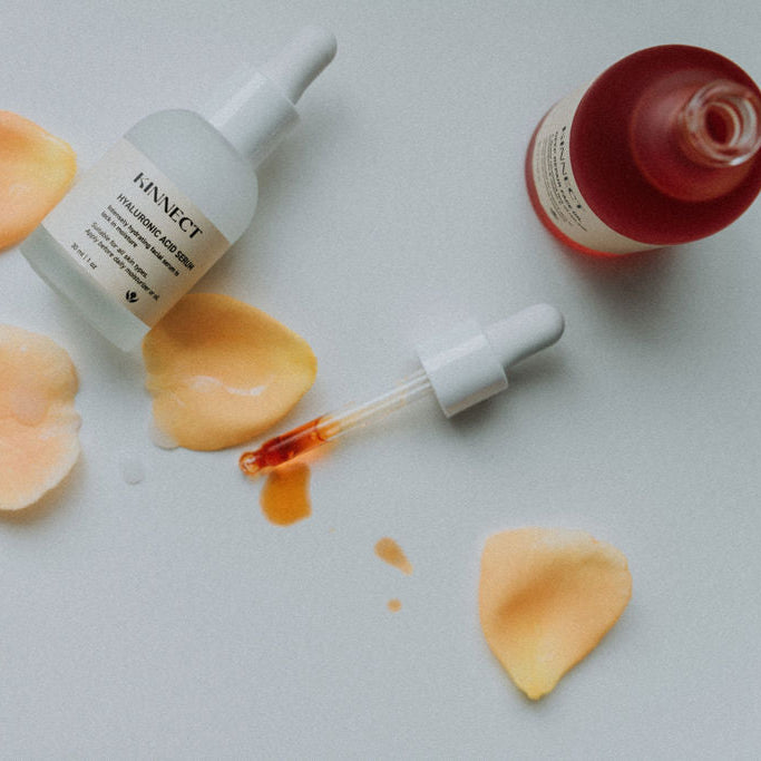 Skincare products with droppers and flower petals on a white background