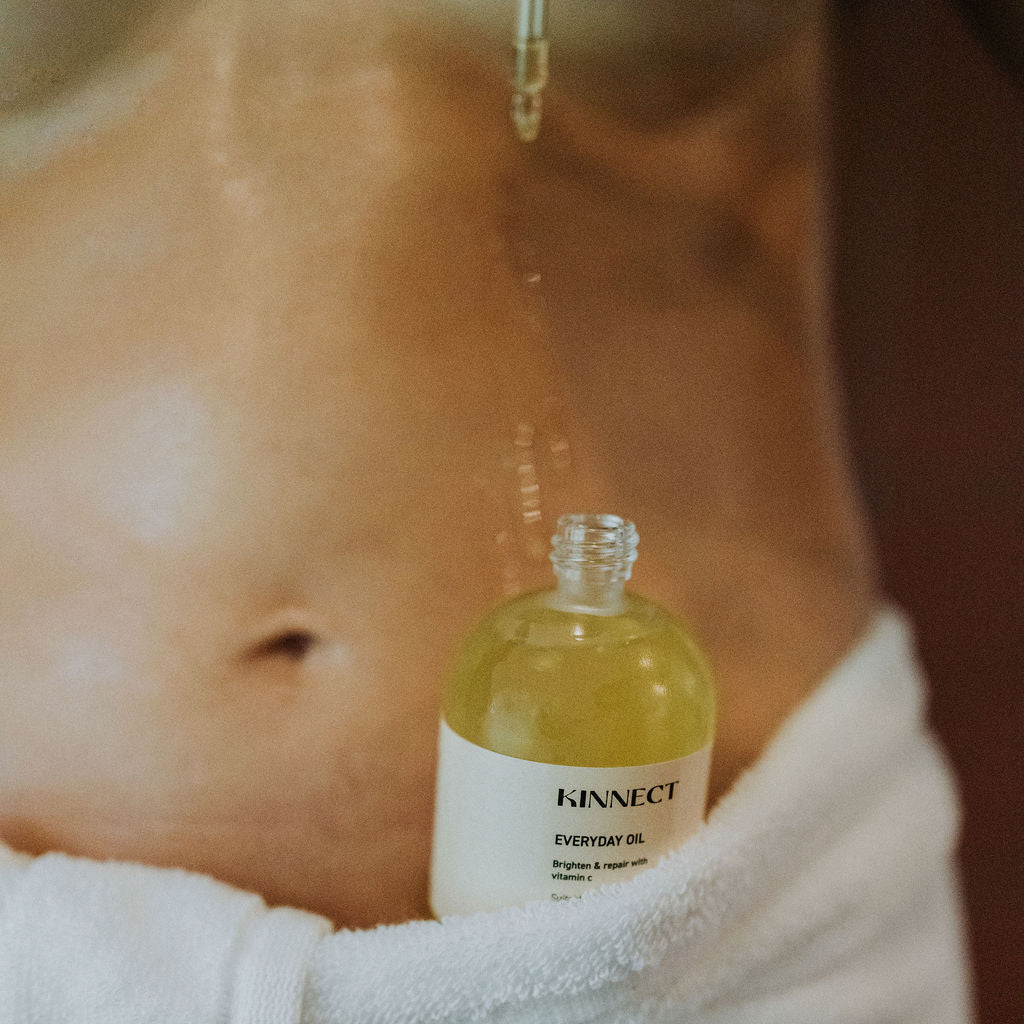 Bottle of kinnect “Everyday Oil” held by a person wrapped in a towel