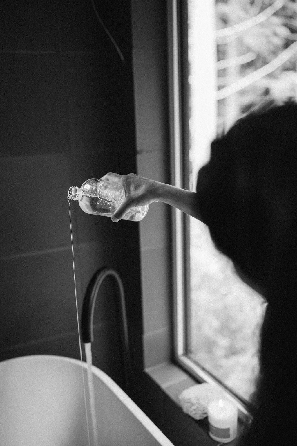 Person pouring a bottle of kinnect bubble bath into their bathtub with running water