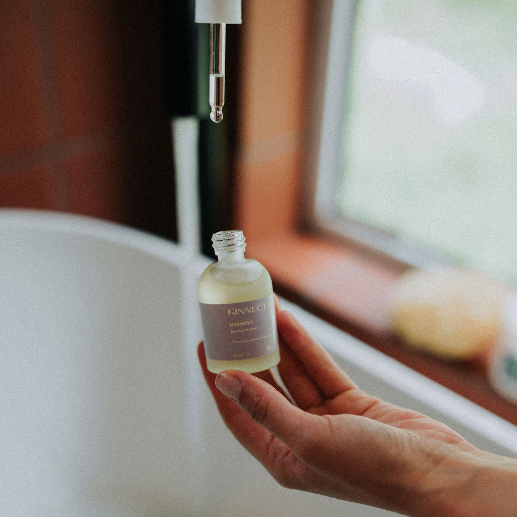 Hand holding a small marmoris essential oil bottle labeled 'KINNECT' with a blurred background