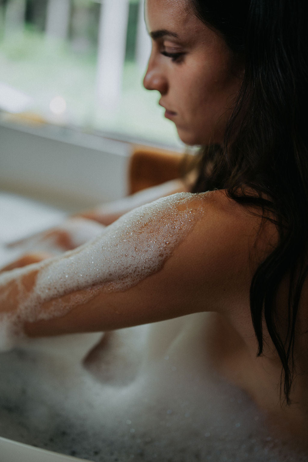 Woman in a bathtub with bubbles, looking down.
