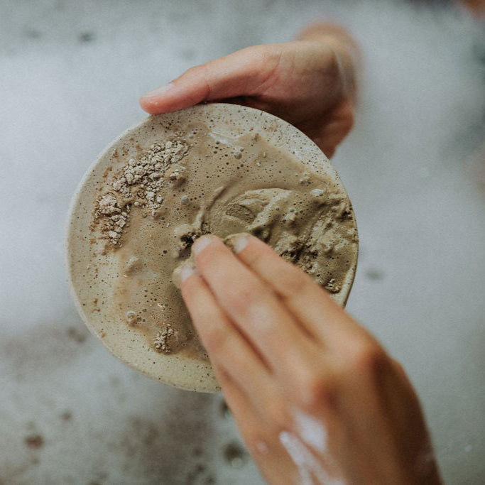 Hand holding a round, textured stone over a soapy water background