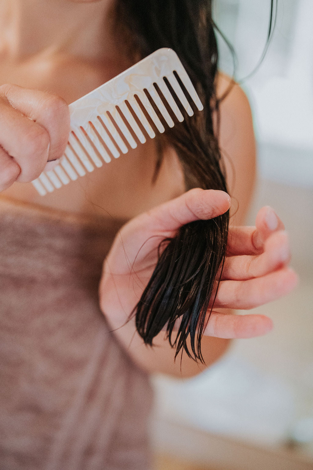 Person combing hair with a white comb in a bathroom setting
