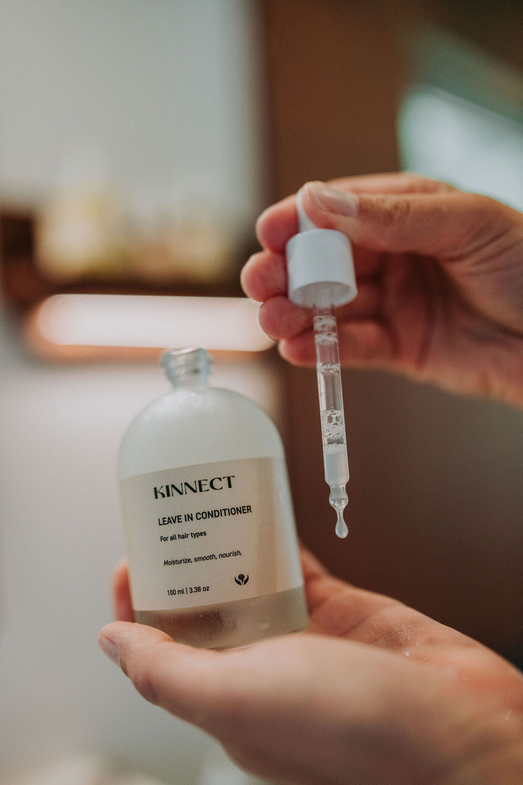 Hand holding a bottle of Kinnect Leave-In Conditioner with a dropper.