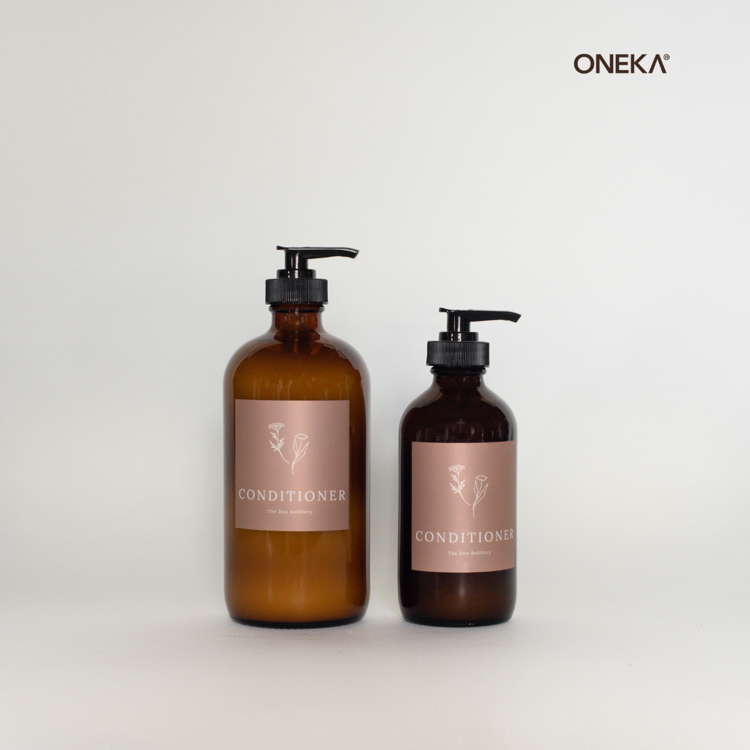 Oneka lavender conditioner in The Den Refillery signature amber glass bottles and pink labels. The conditioner comes in two sizes with pump tops: 500ml [left] and 250ml [right]