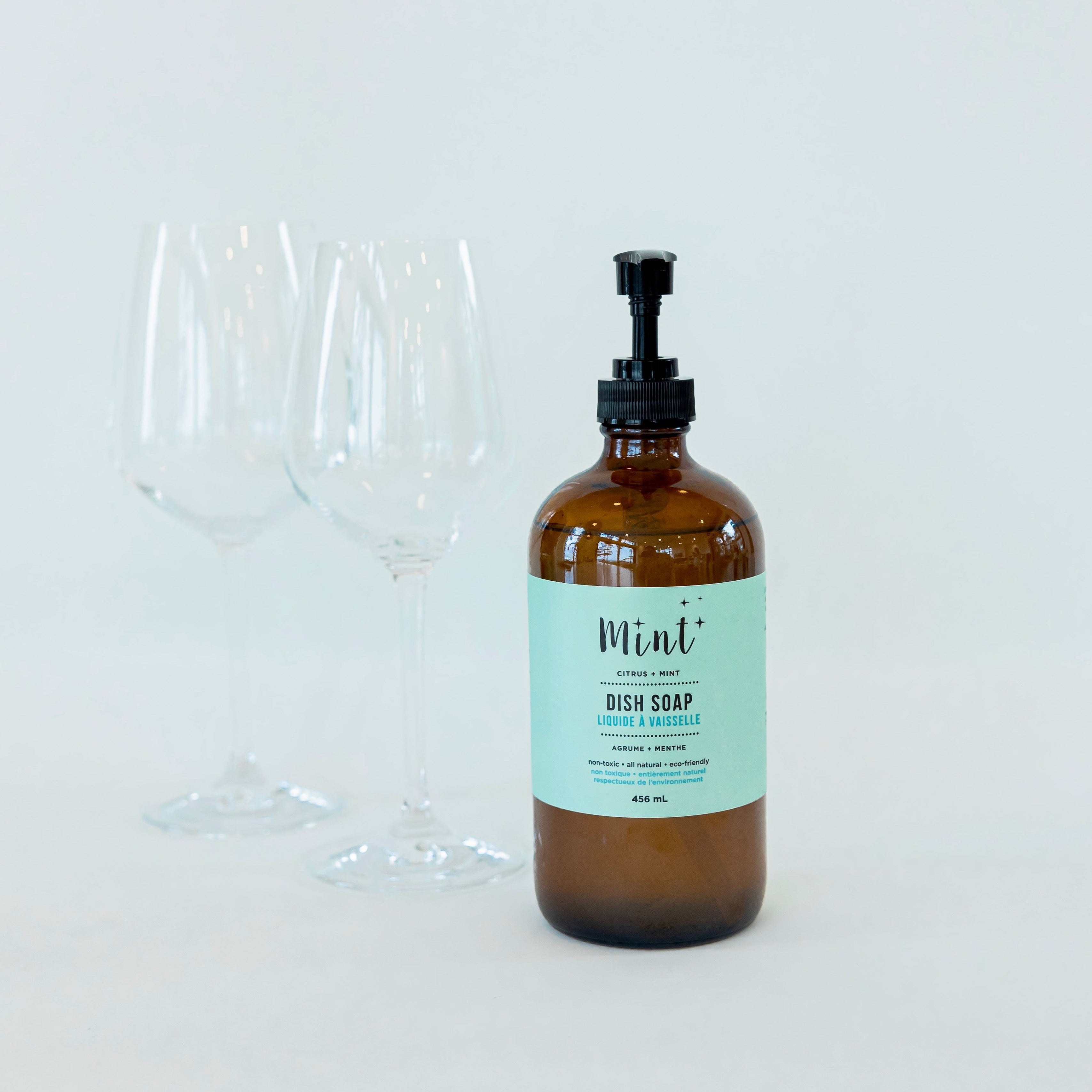 Mint Cleaning co dish soap in an amber glass bottle next to two crystal clear wine glasses