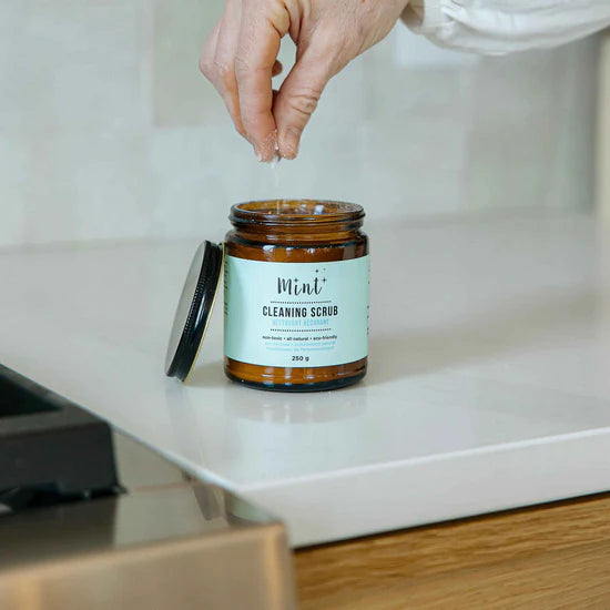 Mint Cleaning Scrub in glass jar on bathroom countertop being sprinkled for cleaning.